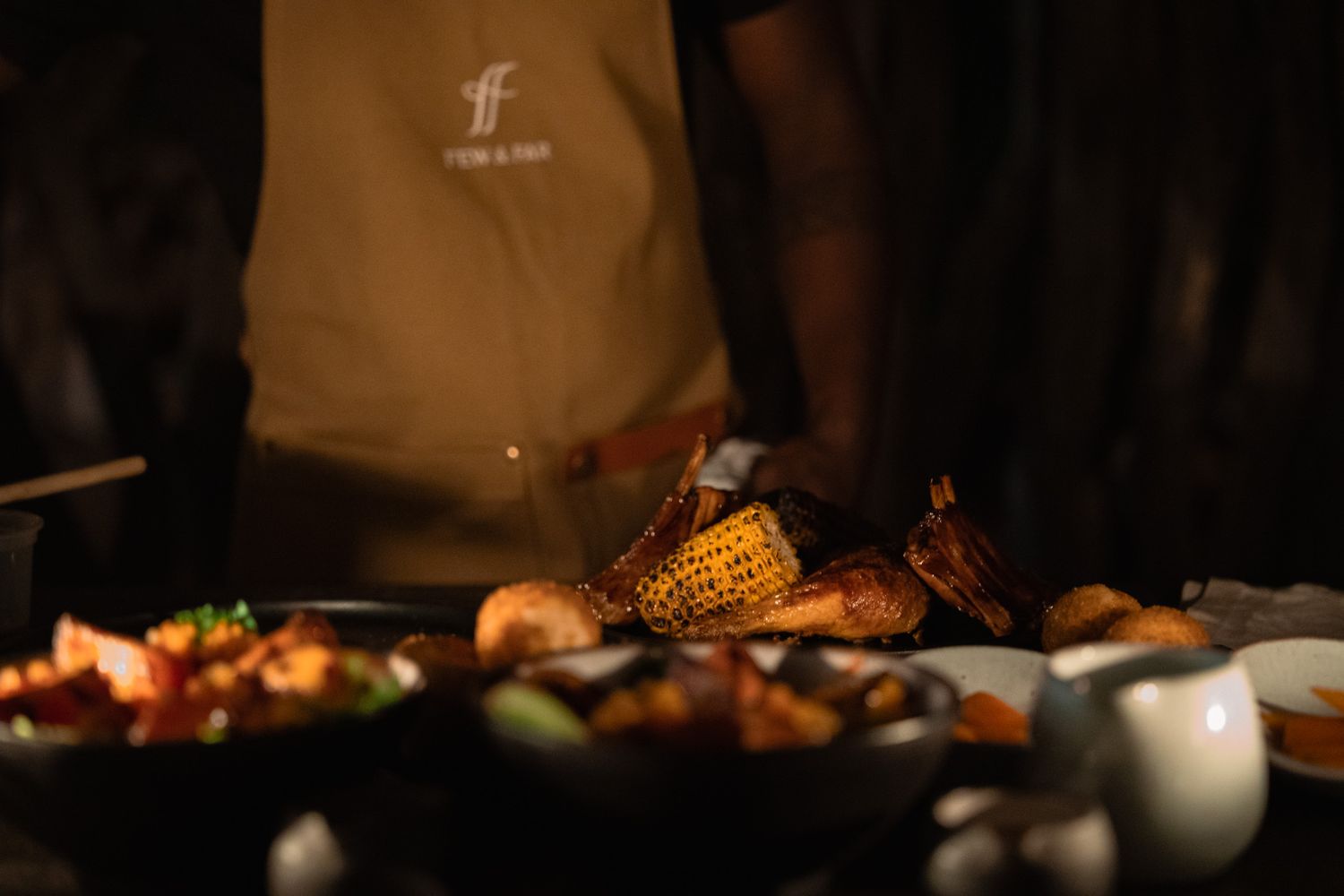 Dimly lit culinary scene showing roasted food and dishes on dark table.