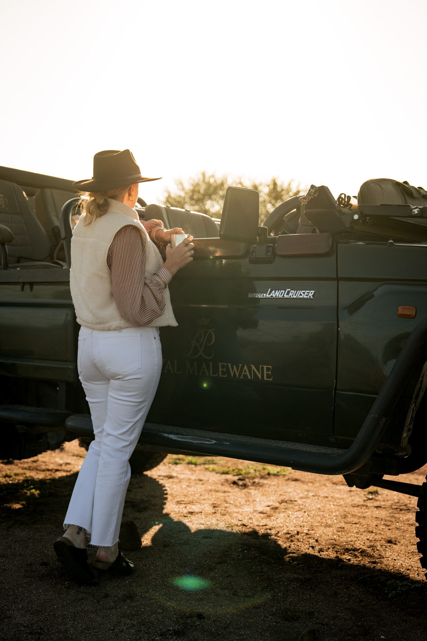 Safari vehicle parked during golden hour at sunset in African wilderness.
