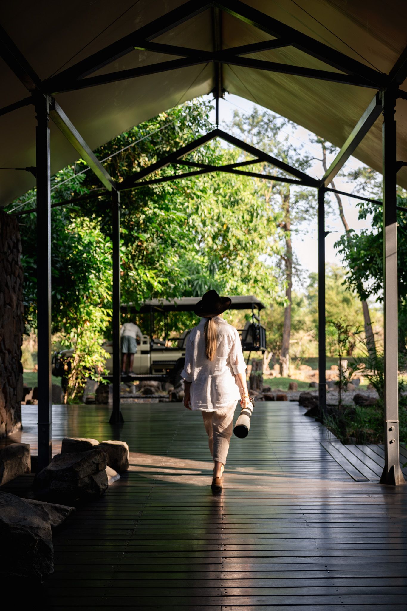Covered wooden deck with sunlight filtering through trees at an outdoor lodge.