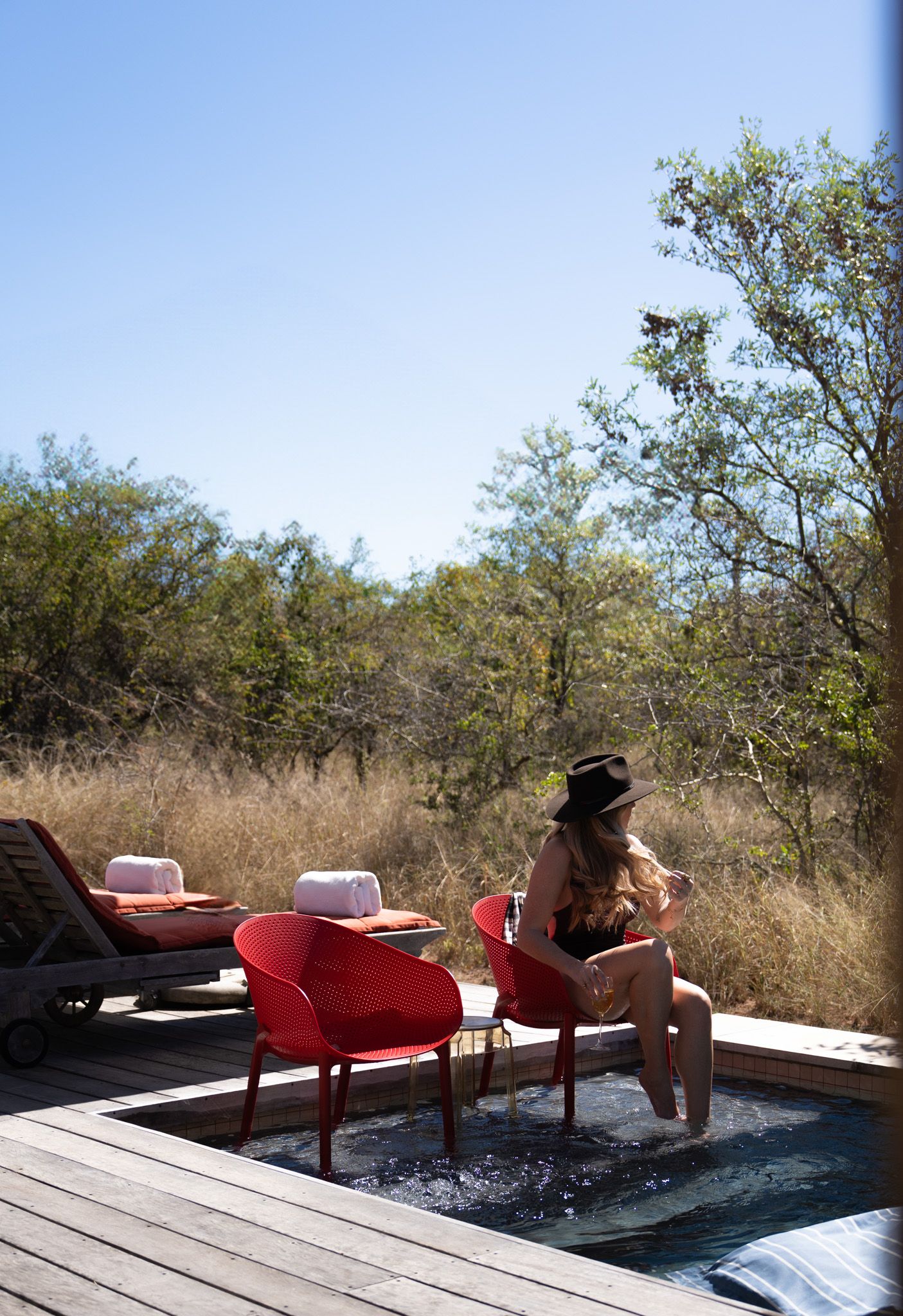 Red lounge chairs on wooden deck with plunge pool overlooking natural landscape.
