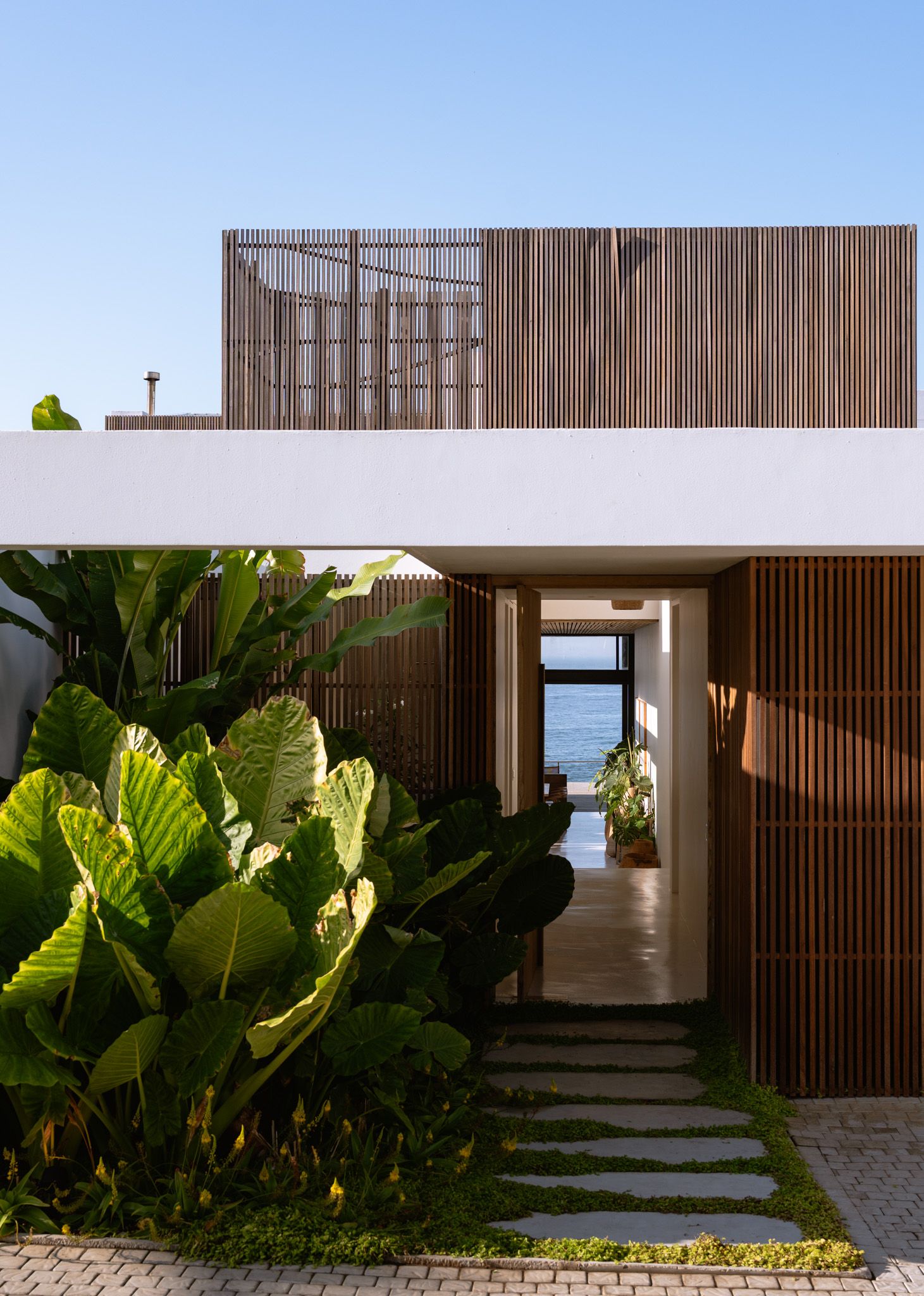 Contemporary beach house entrance with wooden slats and tropical landscaping leading to ocean views.