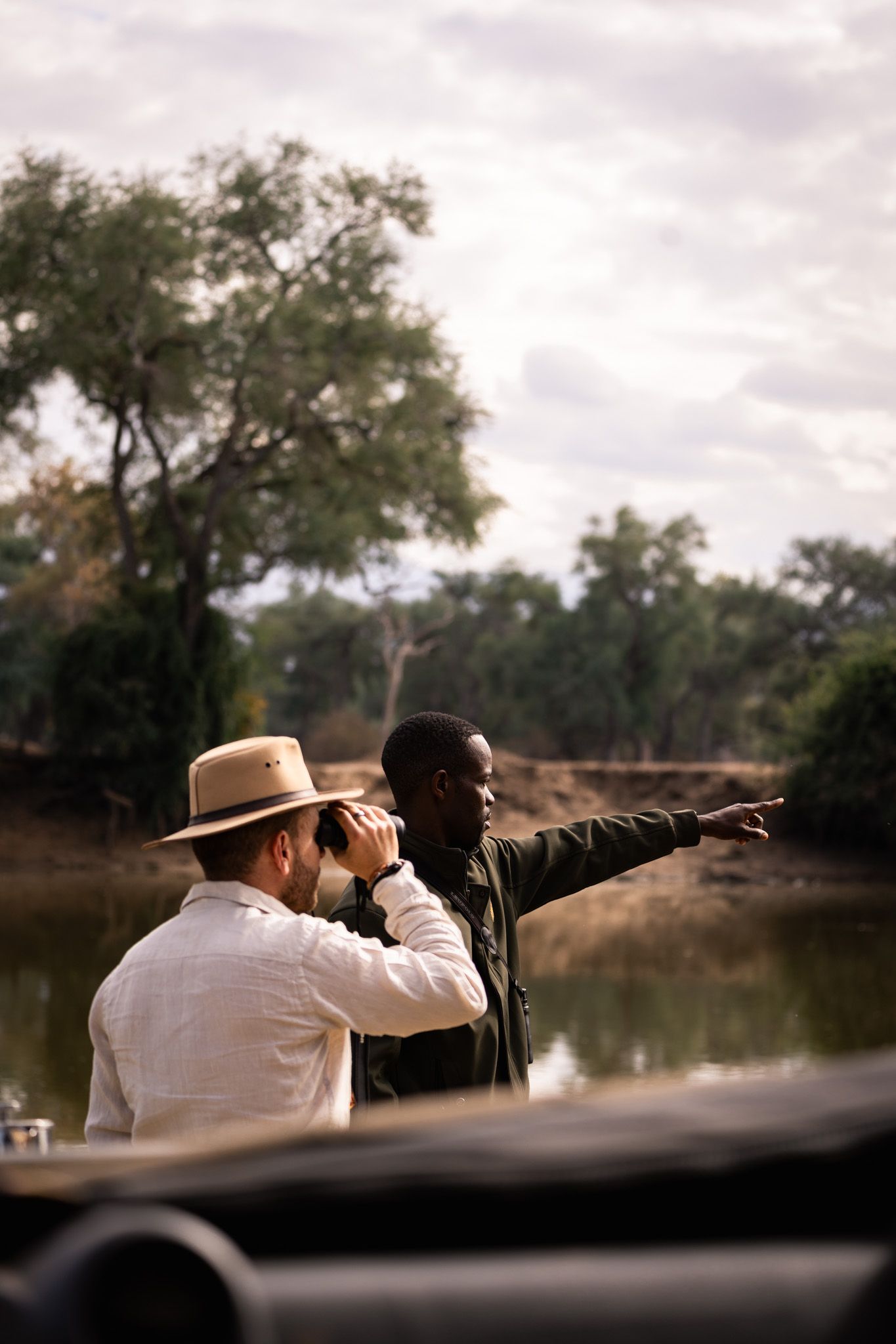 Safari guides spotting wildlife along riverbank during nature tour.