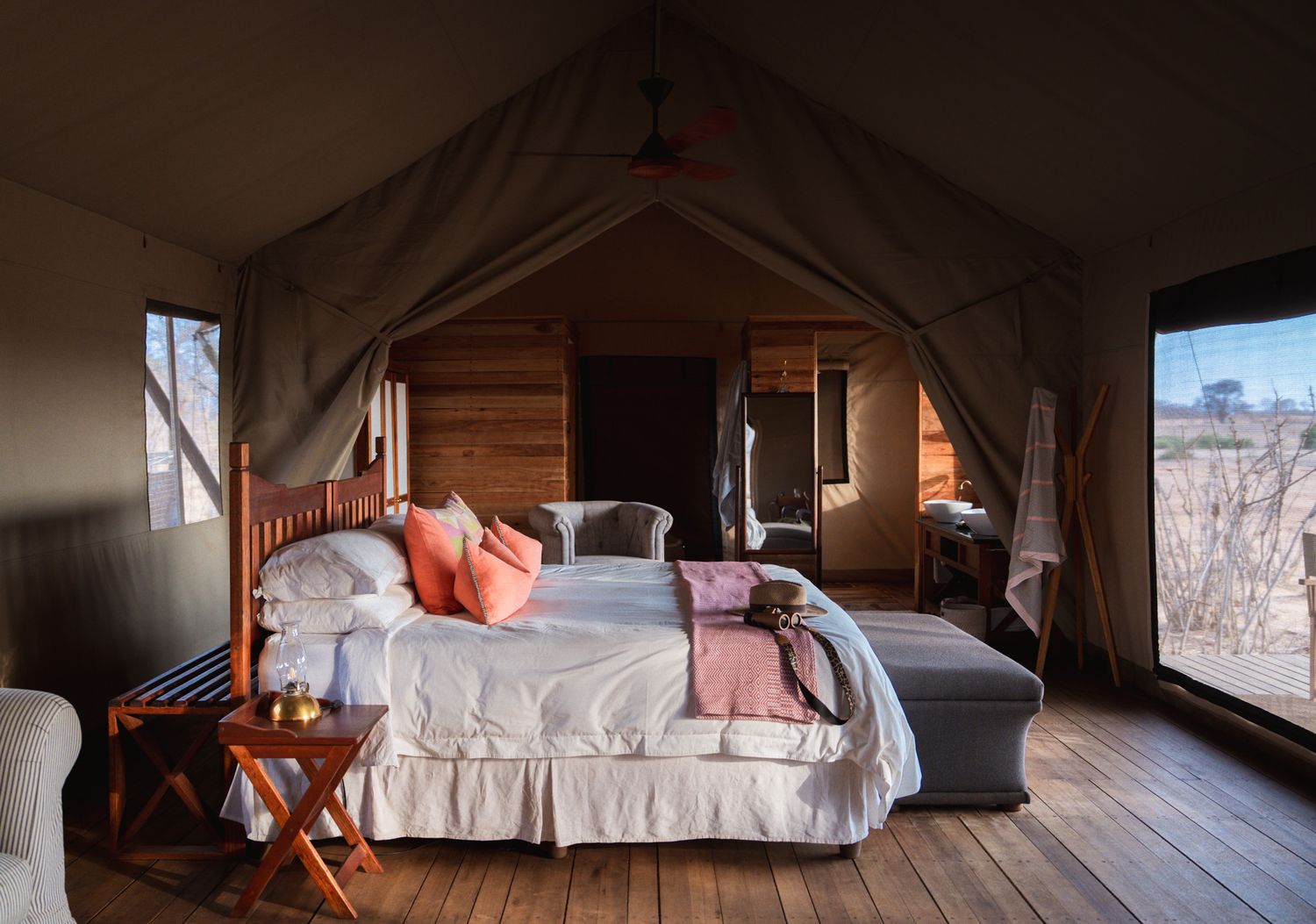 Rustic glamping tent interior with wooden floors and coral accent pillows.
