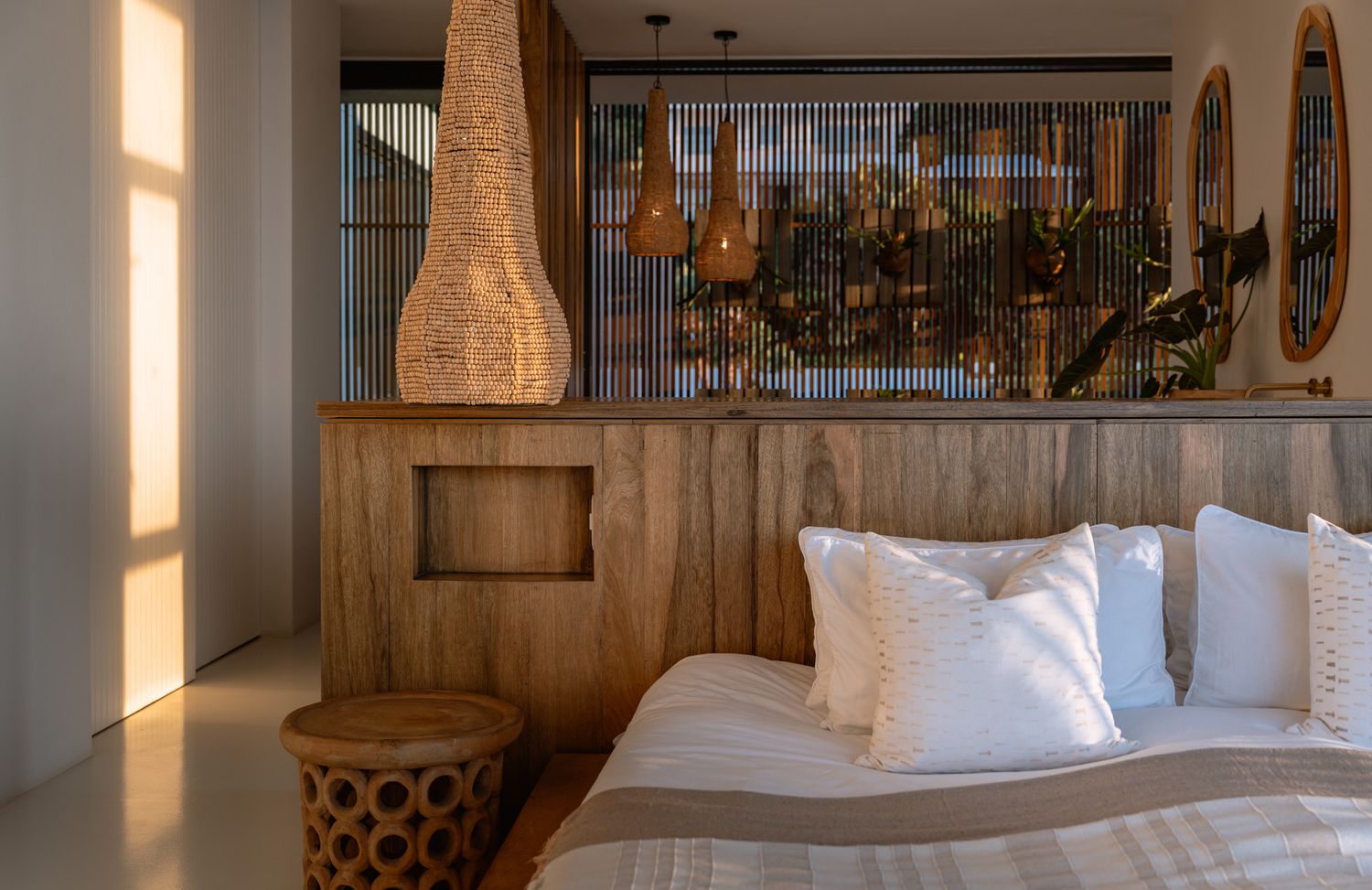 Cozy bedroom corner with natural wood accents, woven pendant light, and white bedding.