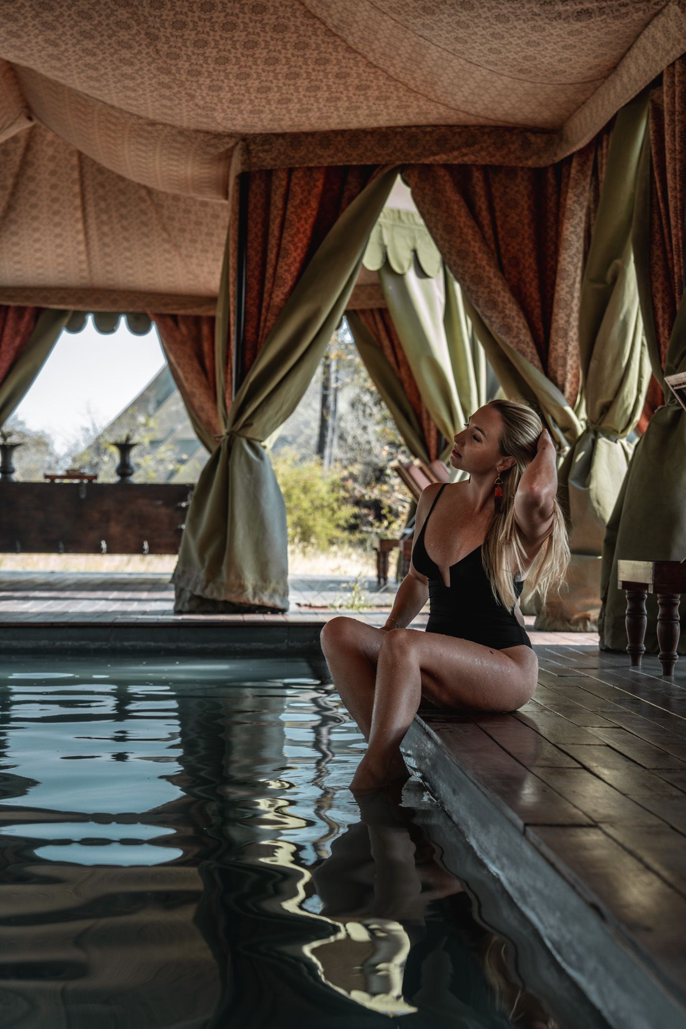 Luxurious pool area with draped fabric ceiling and relaxing guests at the water's edge.