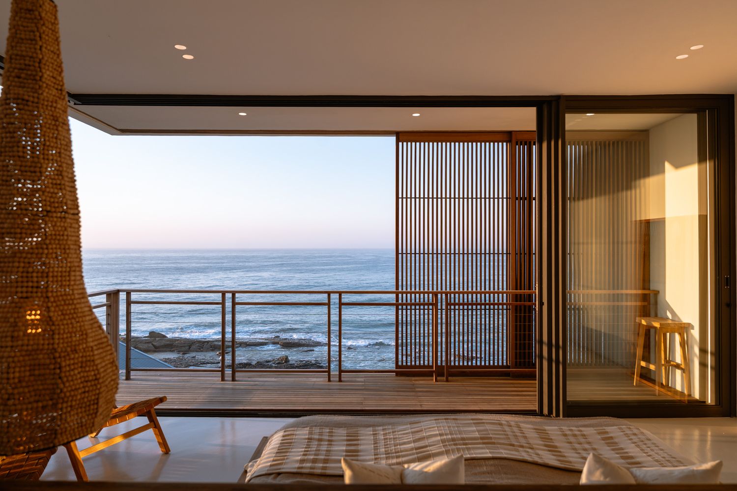 Oceanfront bedroom with floor-to-ceiling windows and wooden privacy screens offering stunning sea views.