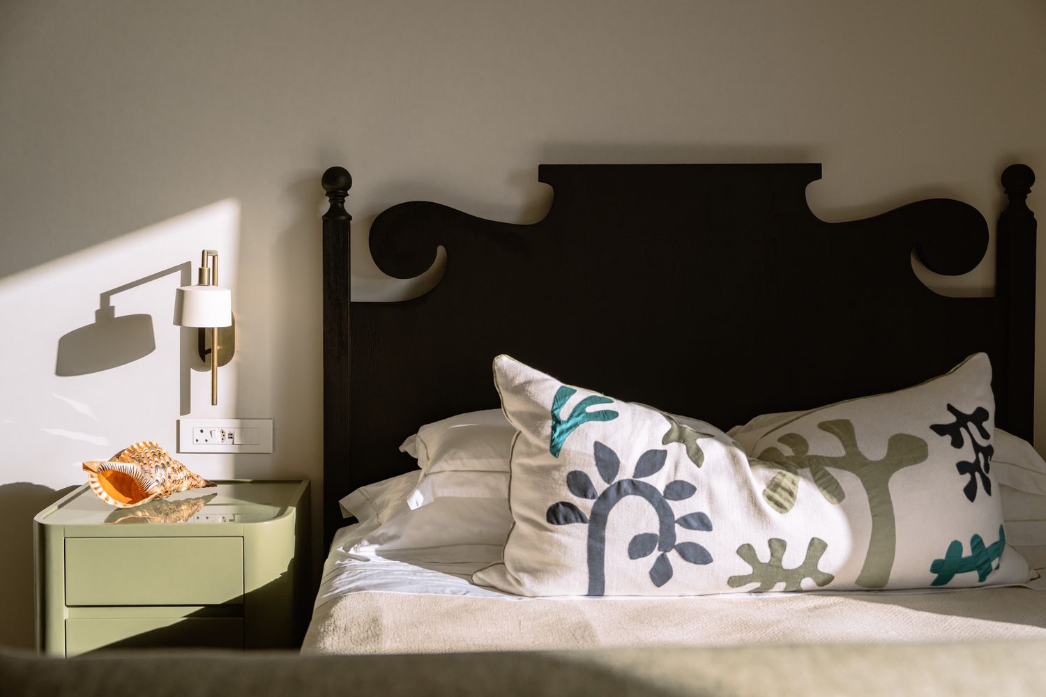 Minimalist bedroom interior with decorative headboard silhouetted against white walls.