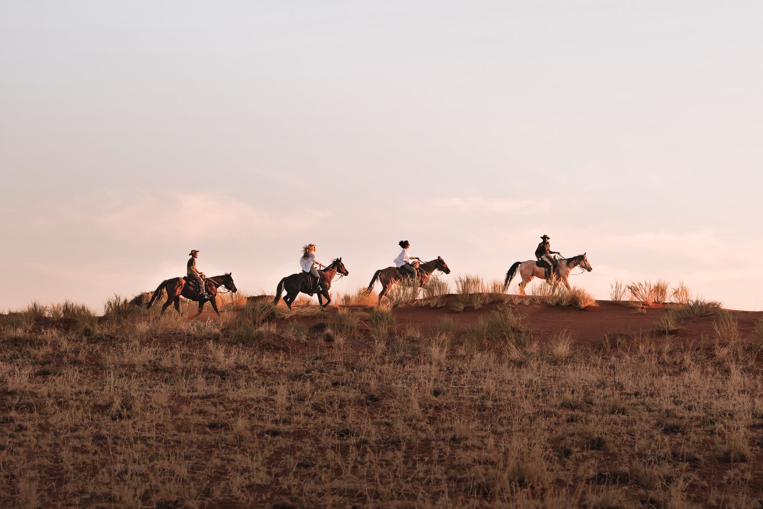 Silhouetted horseback riders traversing along a hilltop during sunset.