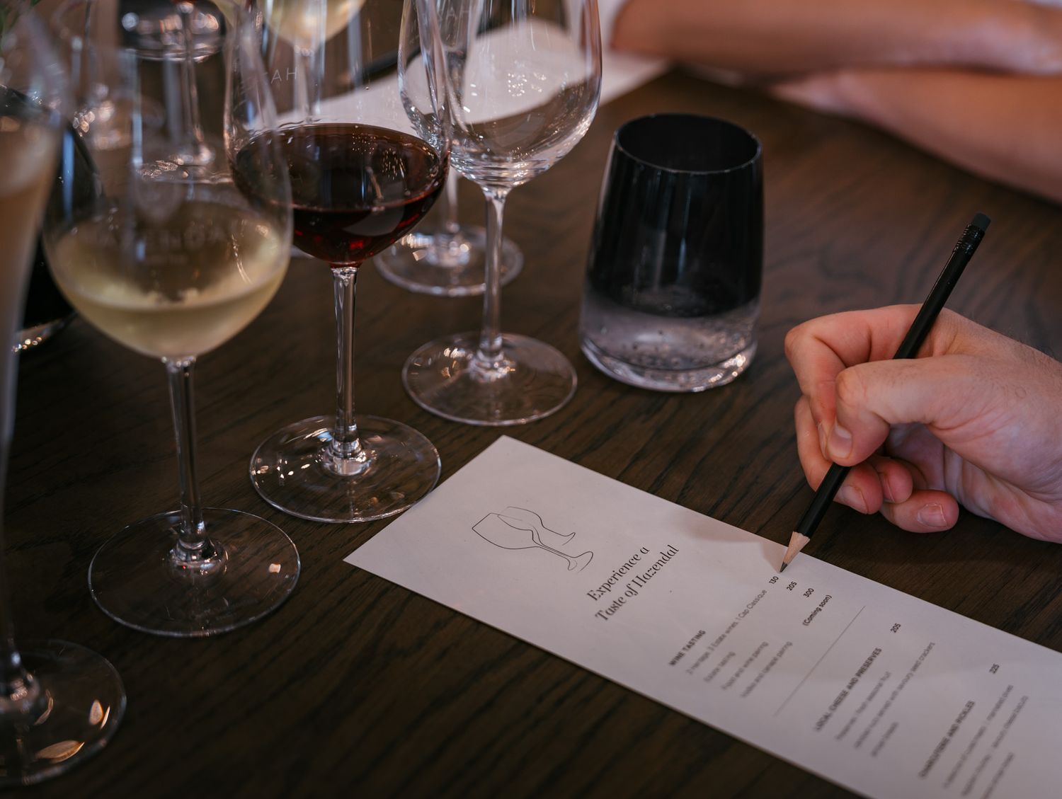 Wine tasting setup with multiple glasses and tasting notes being written on paper.
