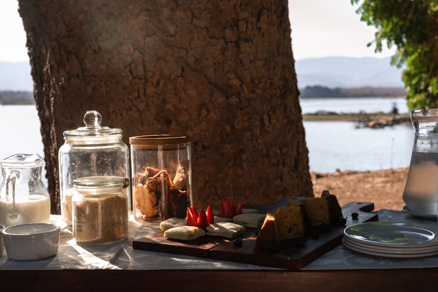 Elegant outdoor table setting with white linens and teacups against an ocean backdrop.