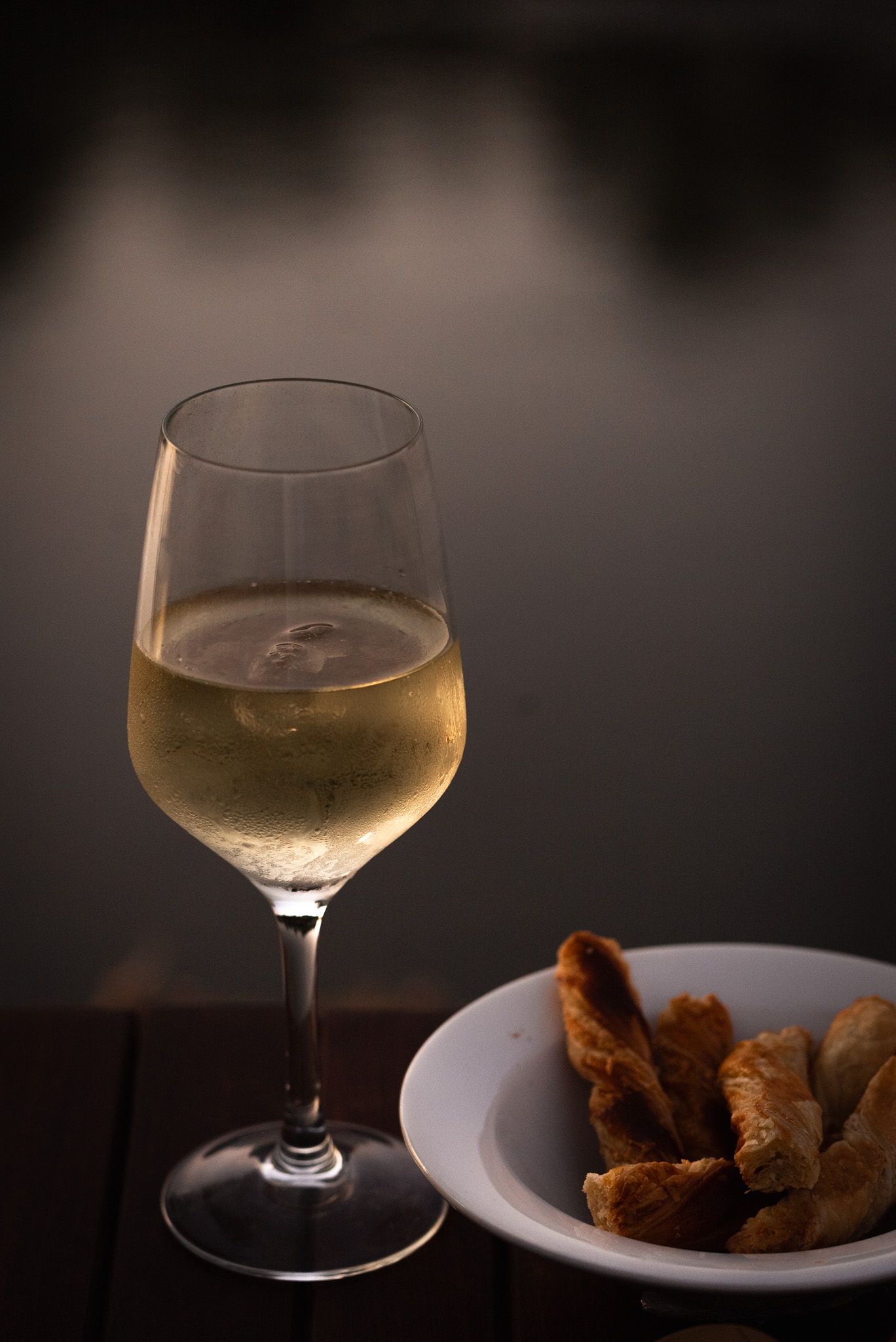 Golden white wine in elegant glasses with appetizers on dark background.