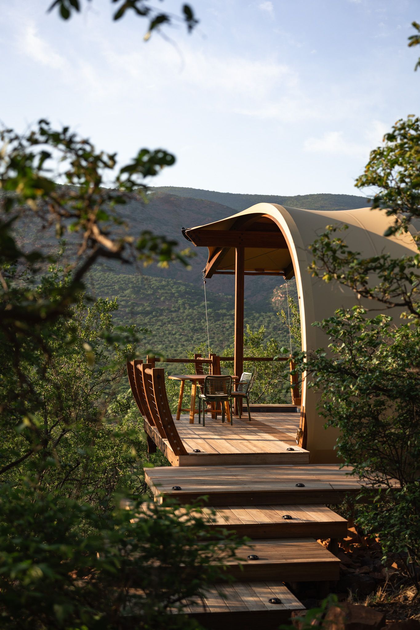 Covered wooden deck platform with outdoor furniture overlooking scenic mountain views through trees.
