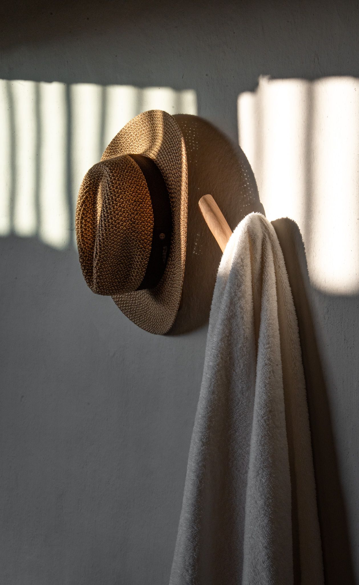 Hat and towel hanging on wall creating dramatic shadows in morning light.