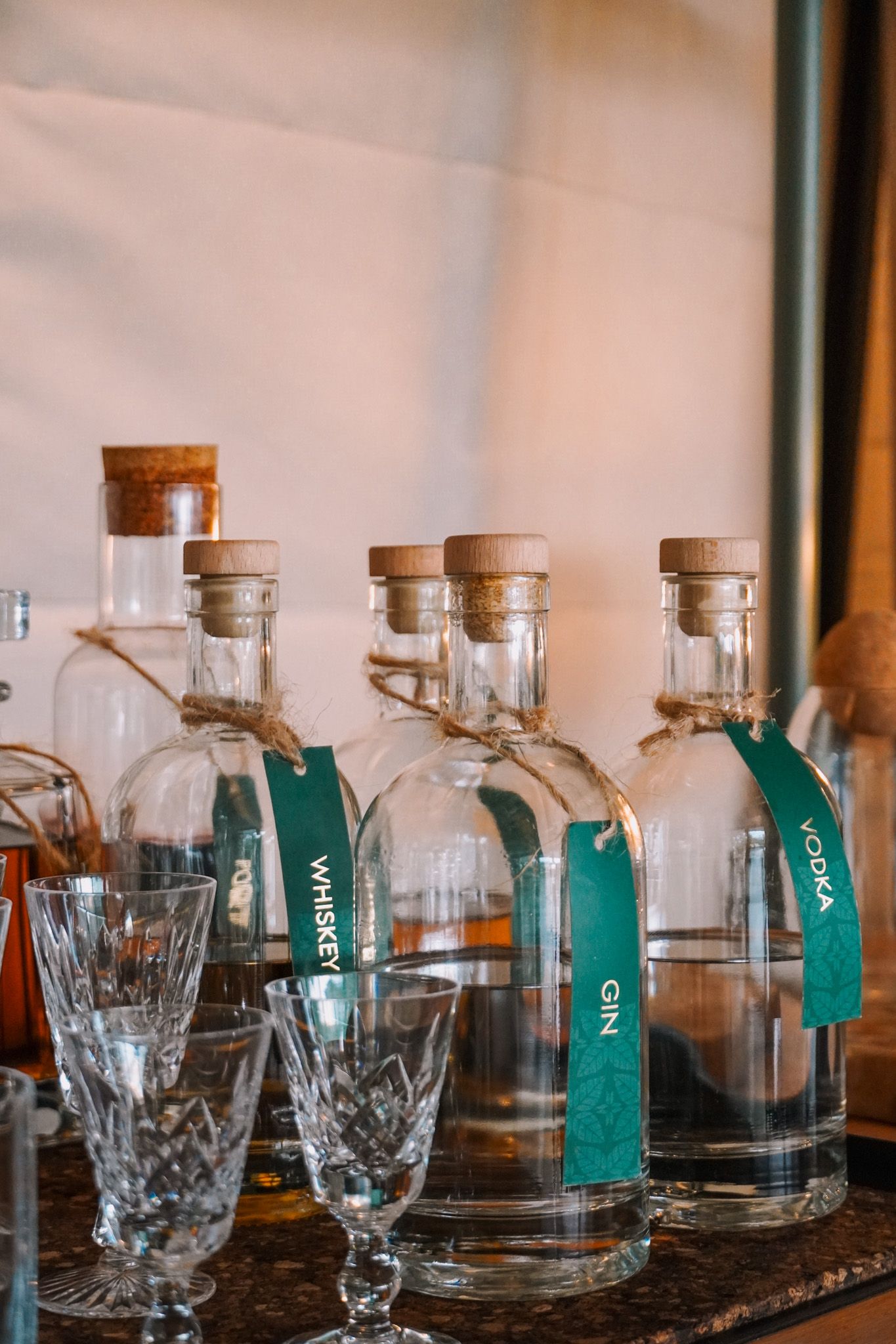 Collection of glass decanters with green labels displayed alongside crystal glasses.