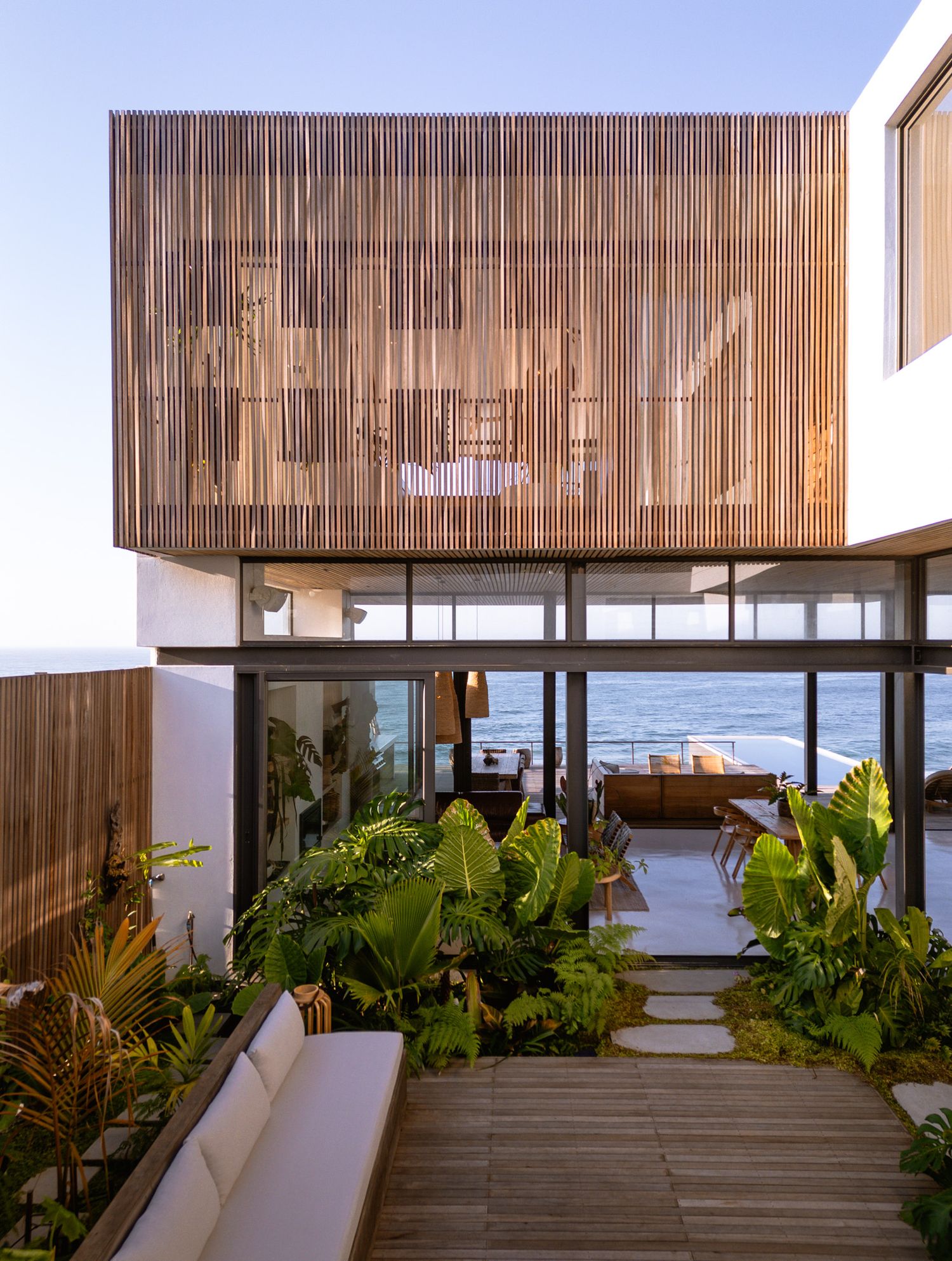 Luxurious covered patio with wooden slats and tropical plants overlooking the ocean.
