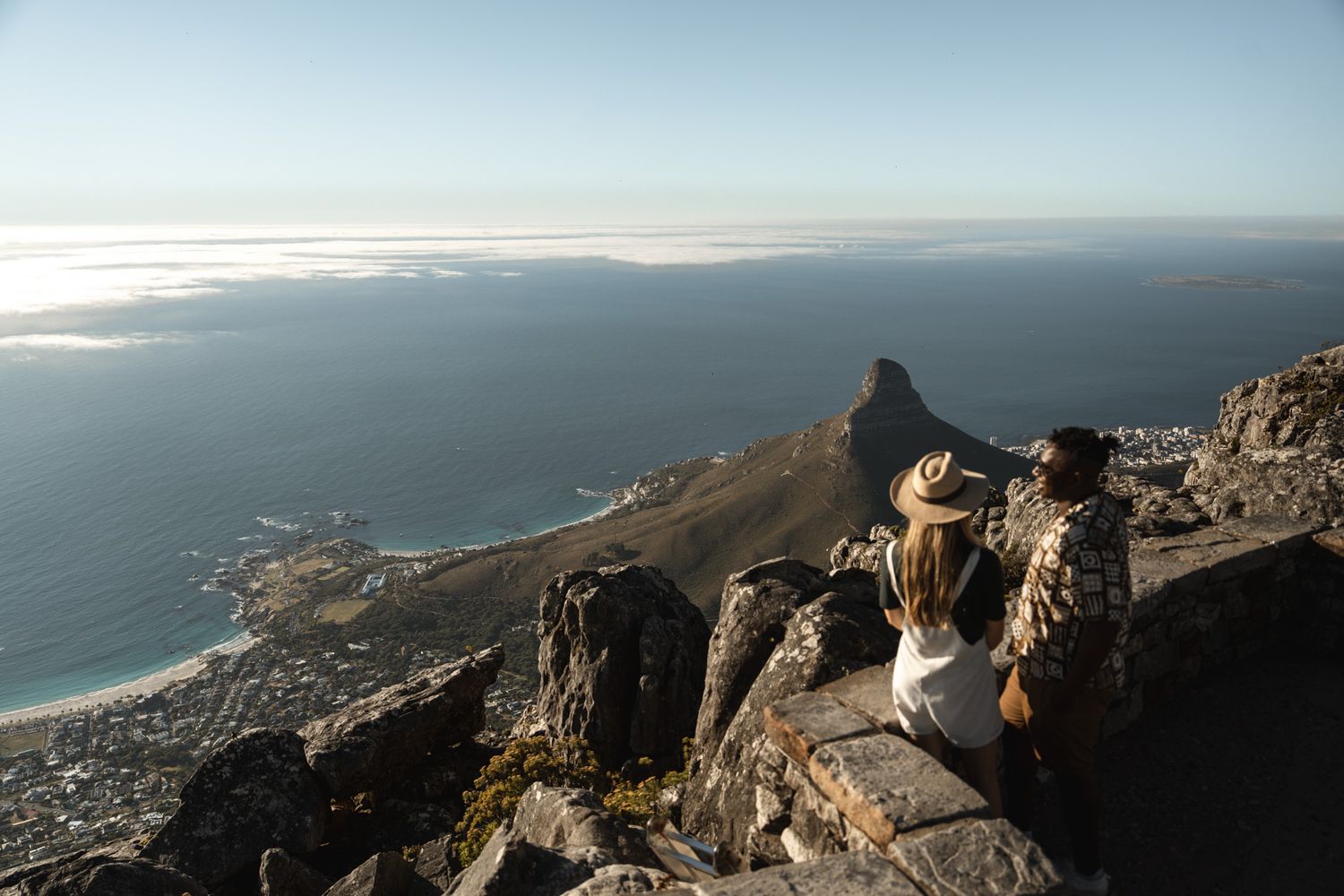 Coastal mountain view with people enjoying panoramic ocean vistas from rocky outcrop.