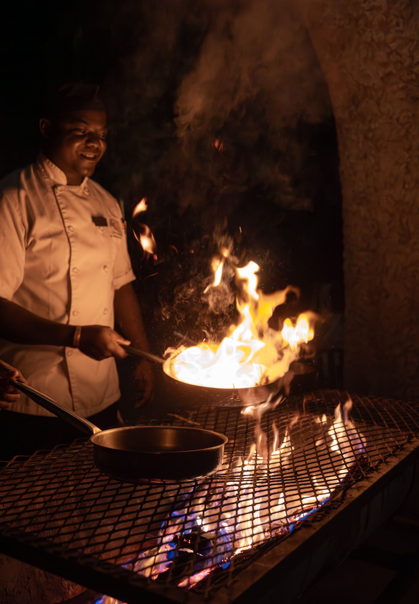 Chef creates flaming dish on outdoor grill at night.