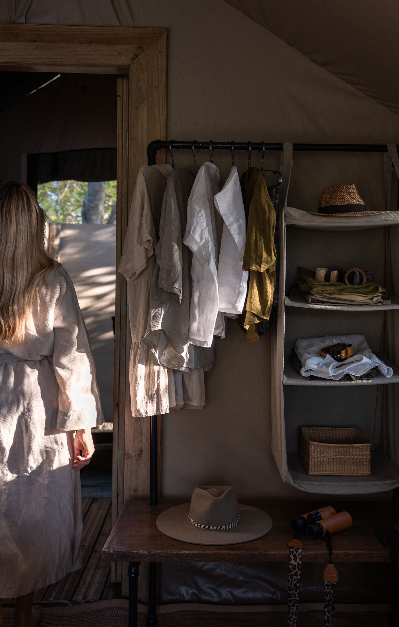 Rustic closet interior with hanging clothes, shelving, and natural sunlight streaming through doorway.