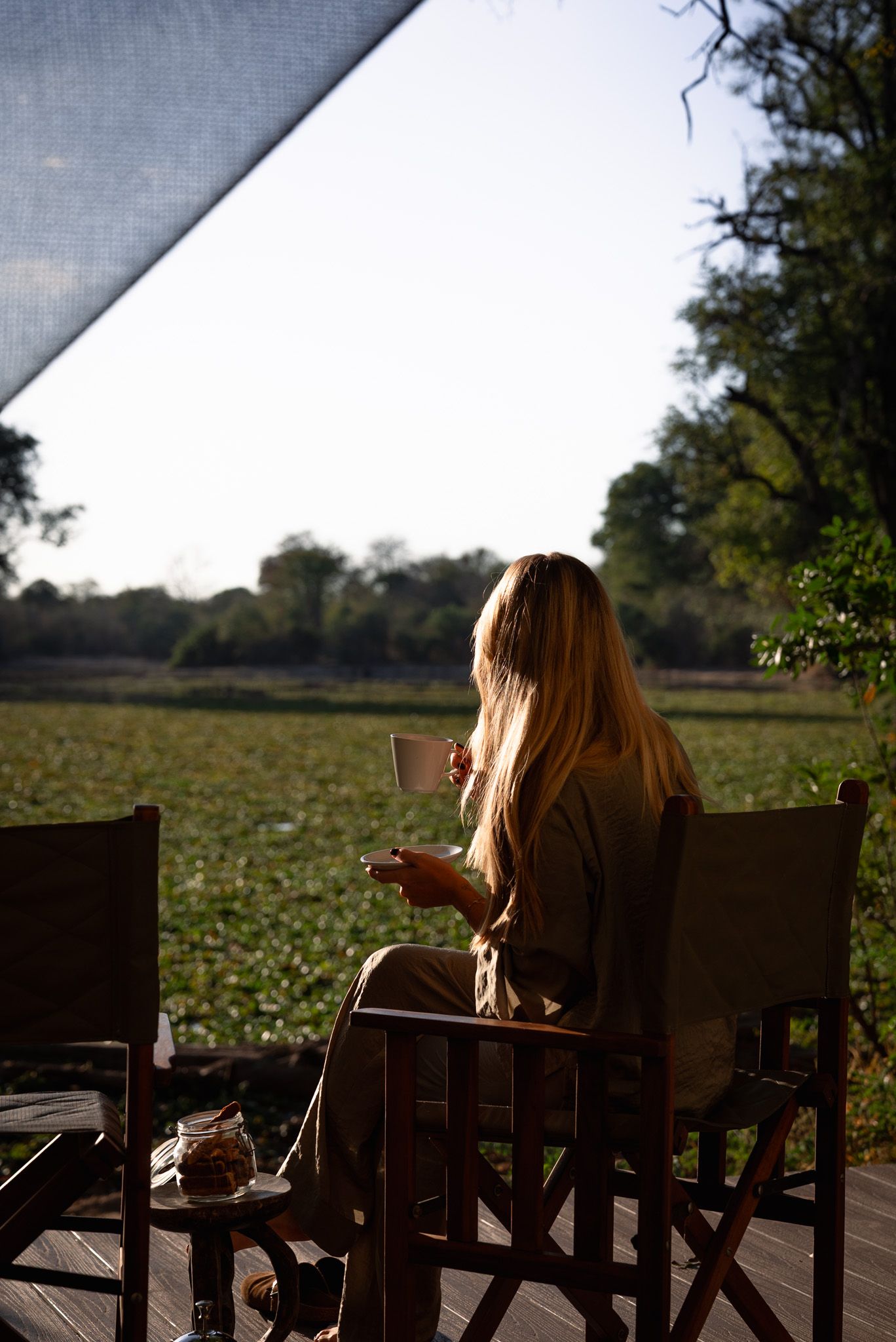Guest relaxes in wooden chair overlooking scenic field at golden hour.