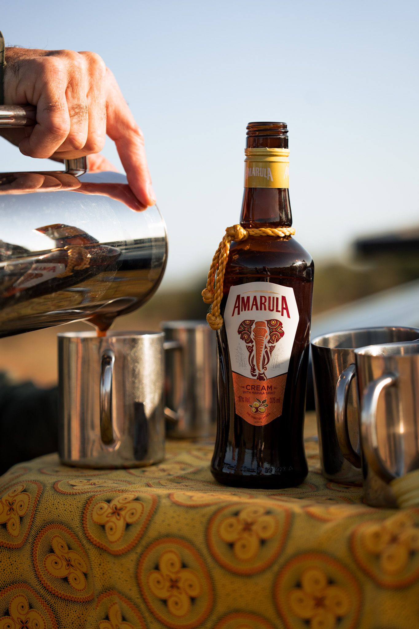 Close-up of Amarula liqueur bottle being poured with mixing equipment on patterned surface.
