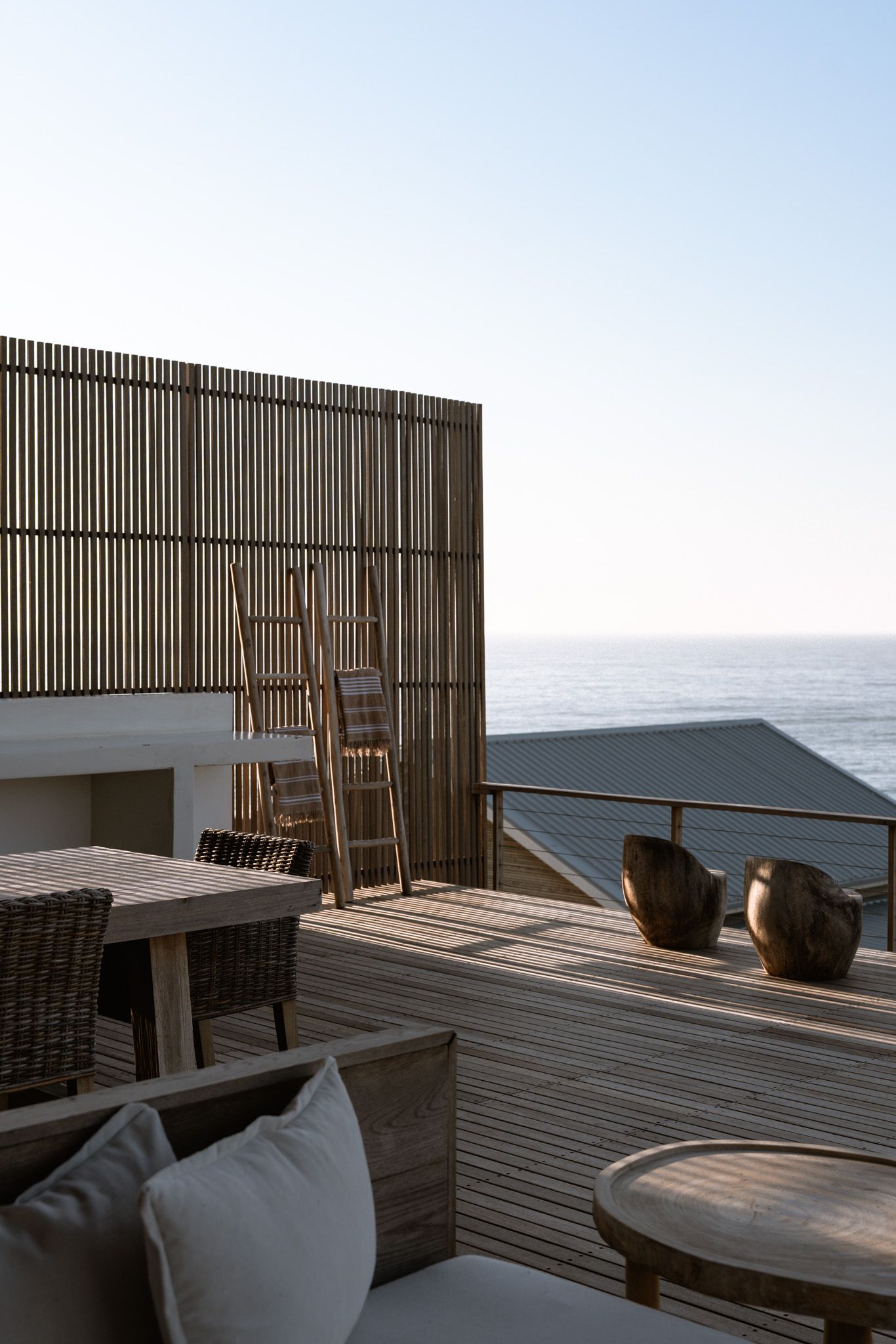 Coastal deck with wooden privacy screen and comfortable outdoor furniture overlooking the ocean.