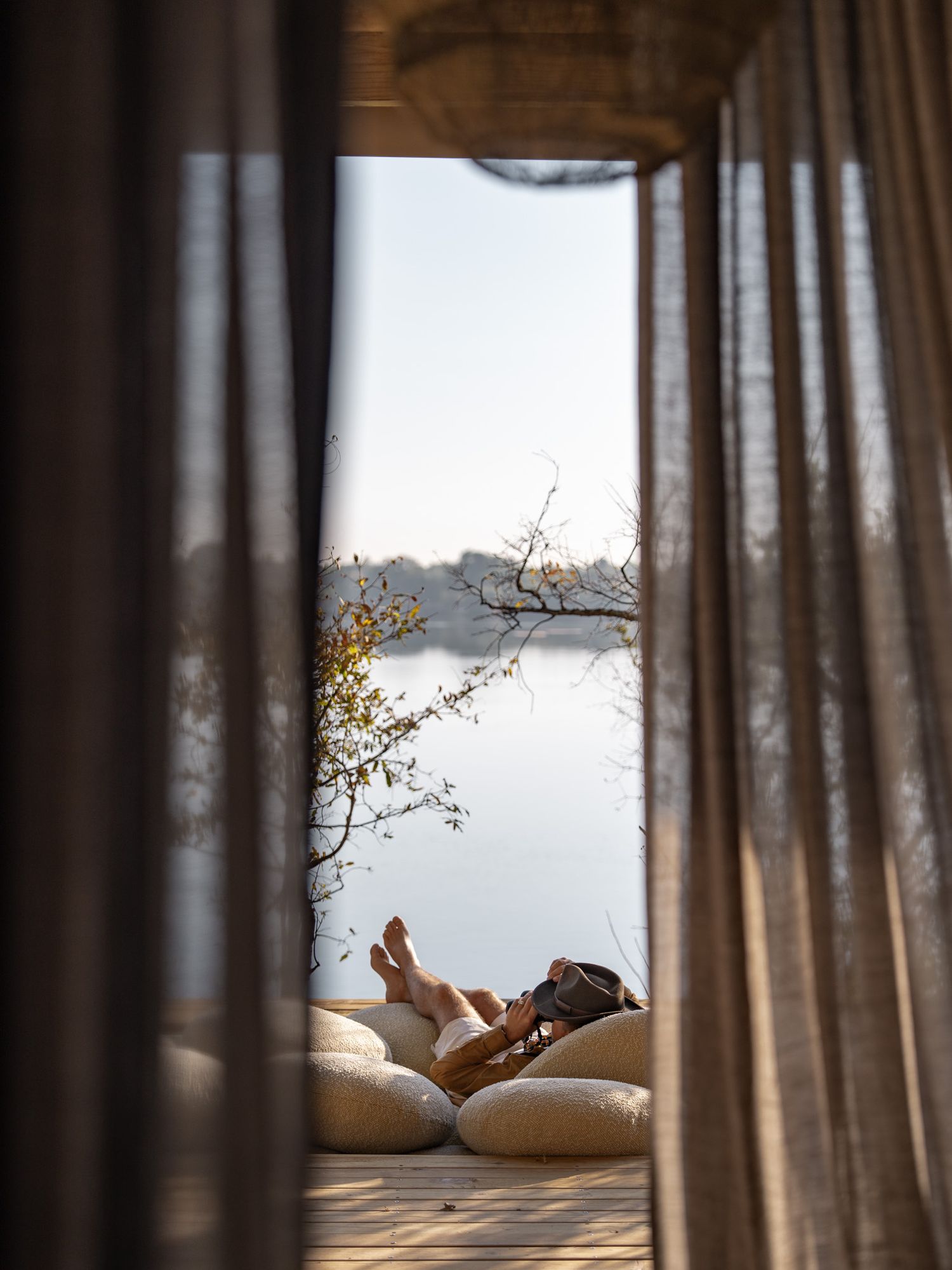 Relaxing lounge area framed by curtains with lake views and plush cushions.