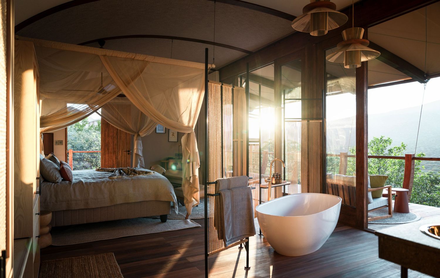 Luxury safari tent bedroom with canopy bed, freestanding bathtub, and panoramic views of lush landscape at golden hour.