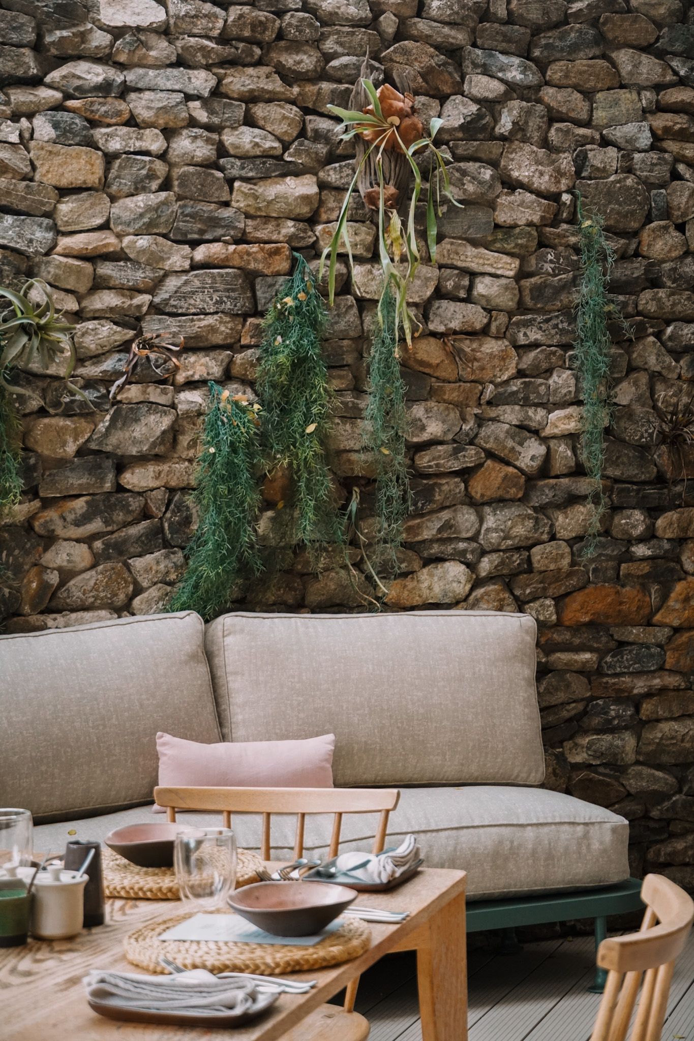 Modern dining setup with beige cushioned seating against a rustic stone wall.