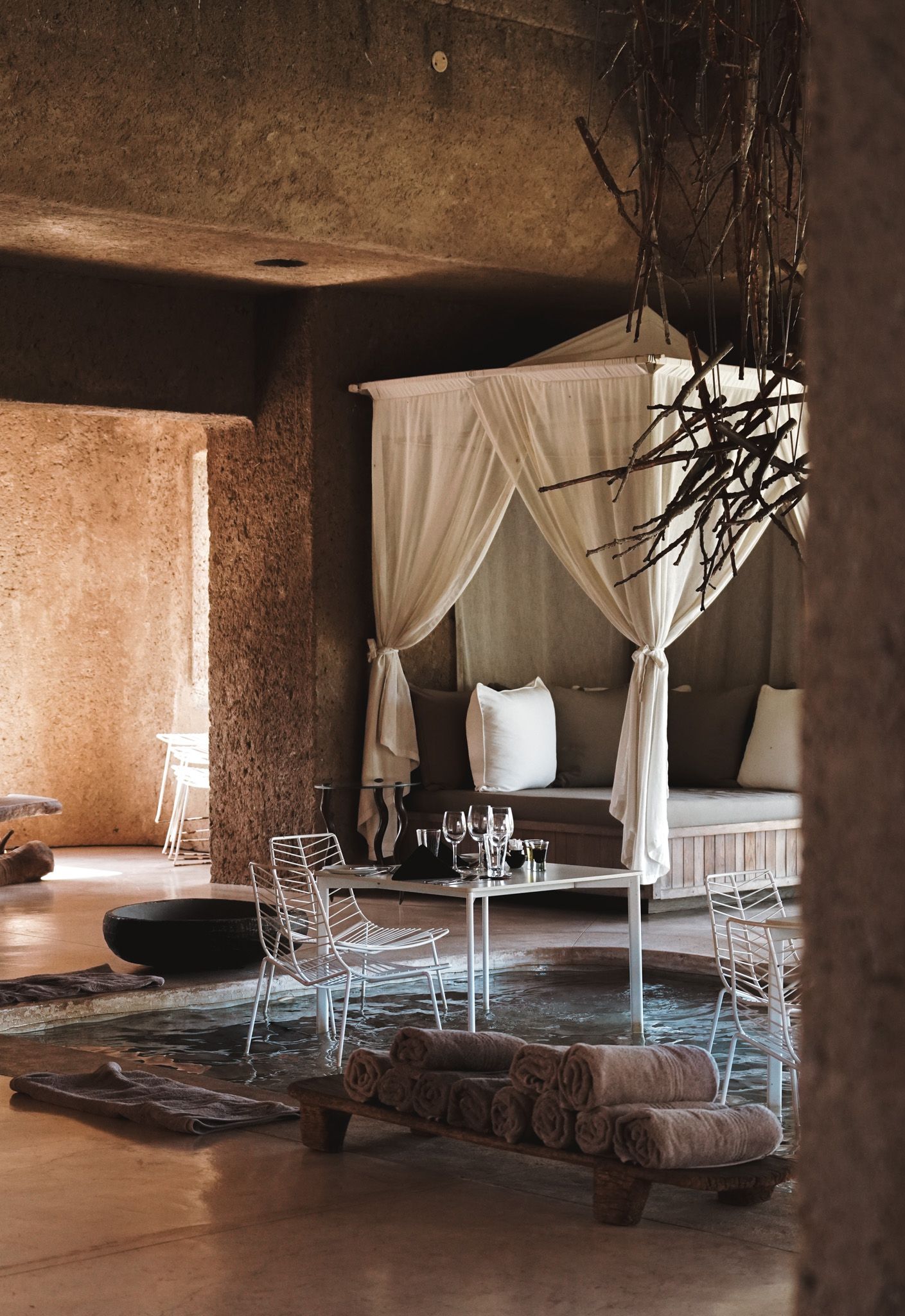 Rustic lounge area with white curtains, wire chairs, and stone walls creating a cozy atmosphere.