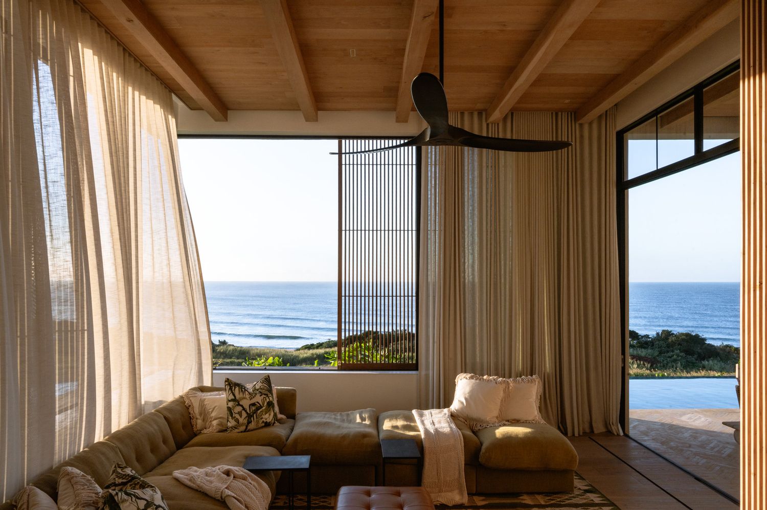 Panoramic oceanfront view through large windows in a modern wooden-ceiling room.