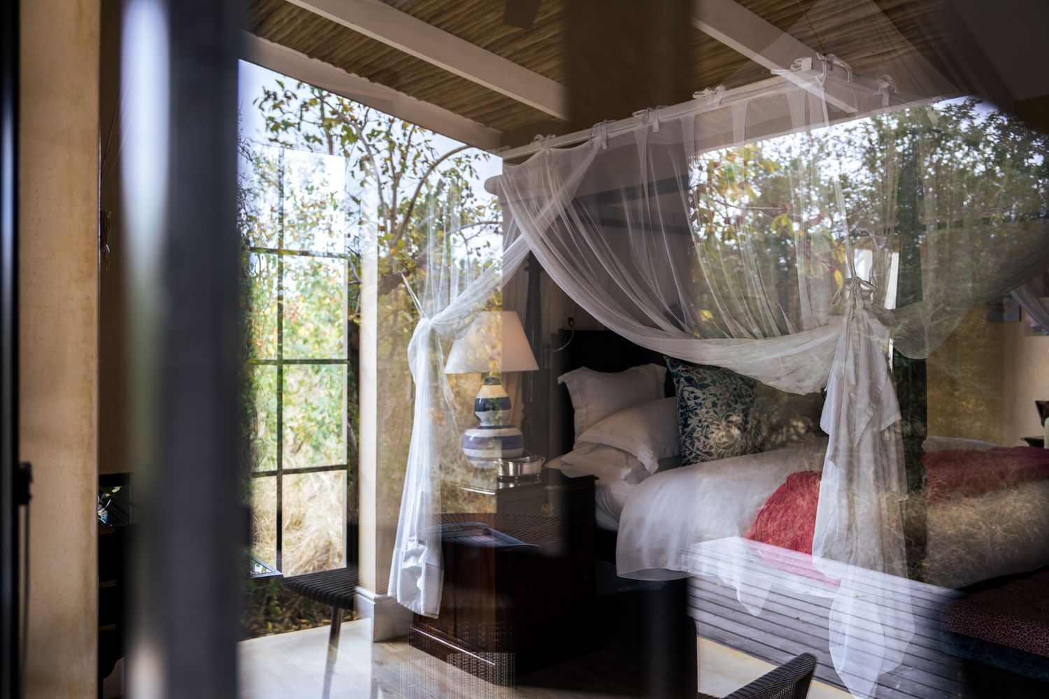 Dreamy bedroom interior with sheer canopy draped over bed and large windows overlooking nature.
