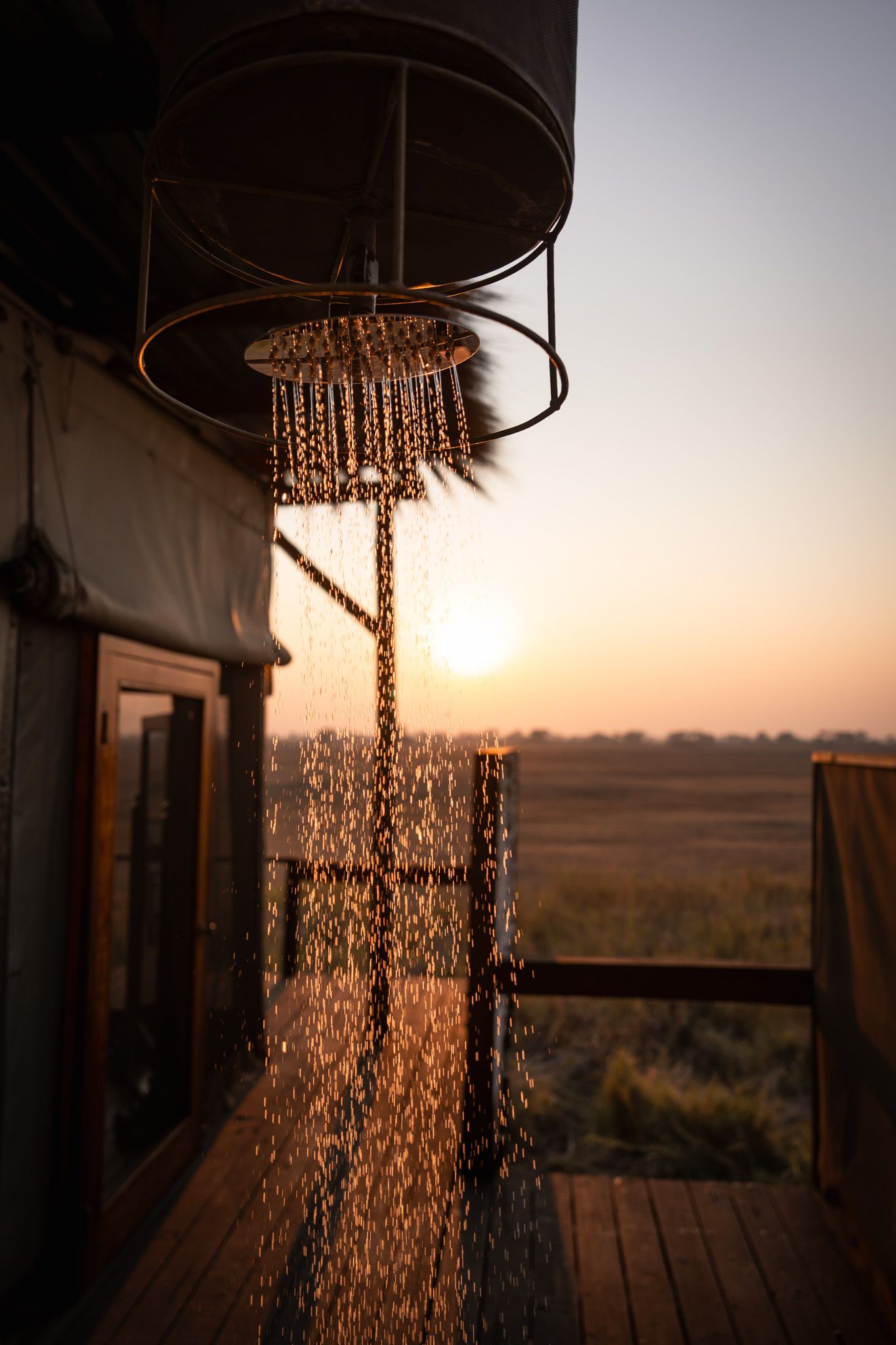 Outdoor shower with water droplets glistening in golden sunset light against natural landscape.
