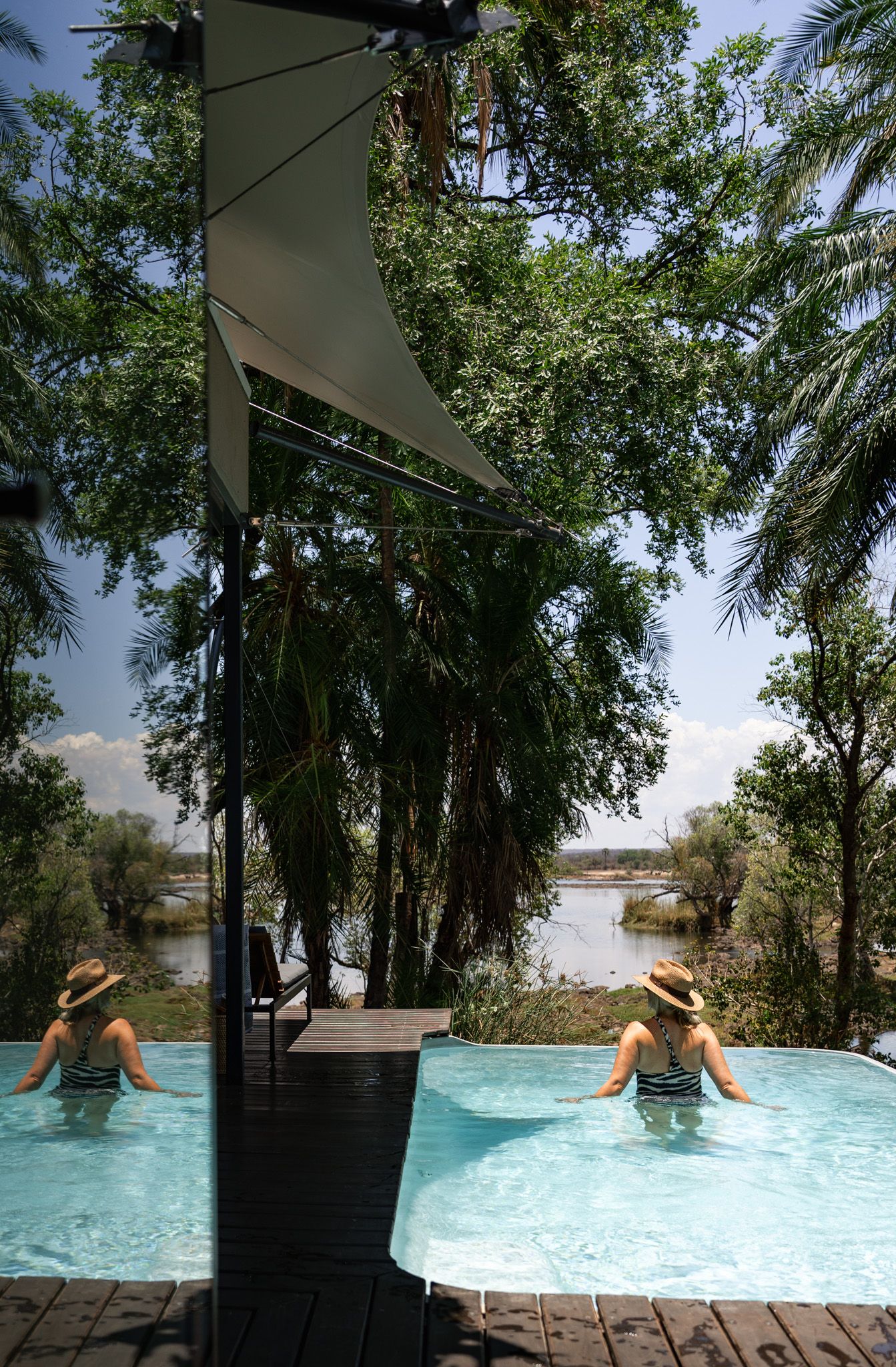 Two infinity pools overlooking a serene lake surrounded by palm trees and natural vegetation.