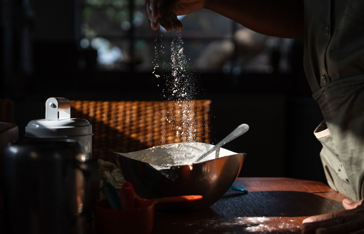 Chef sprinkling ingredients into a copper cooking pot in dramatic lighting.