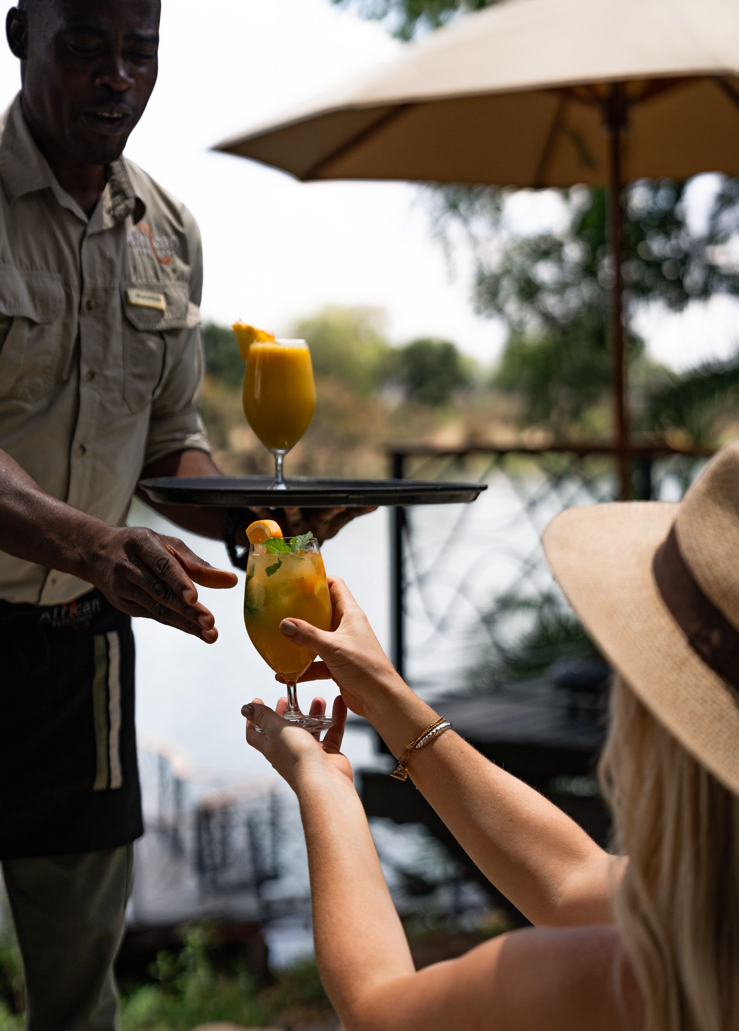 Staff member serving yellow cocktails on a tray outdoors.