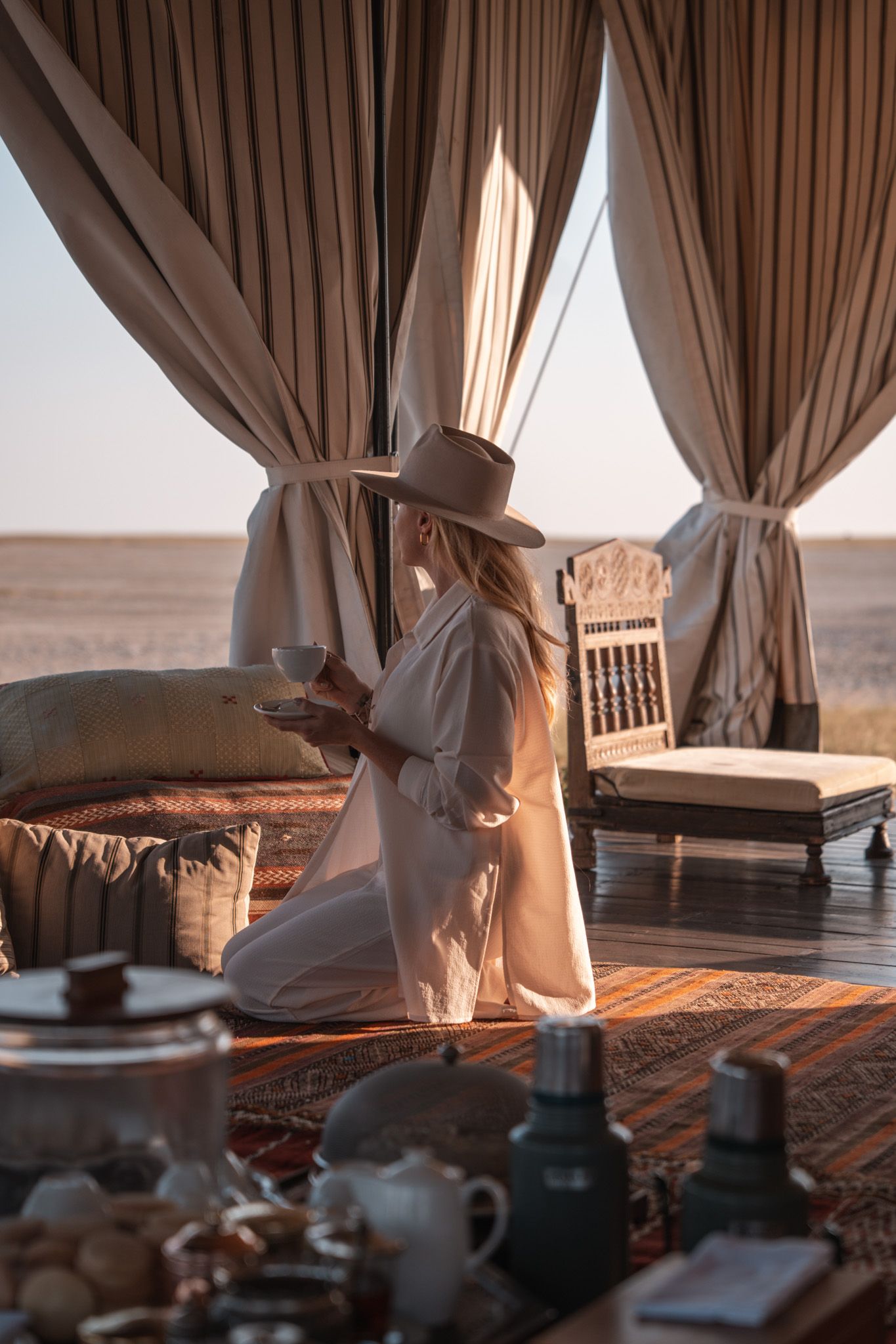 Luxurious safari tent interior with draped curtains and table setting at sunset.