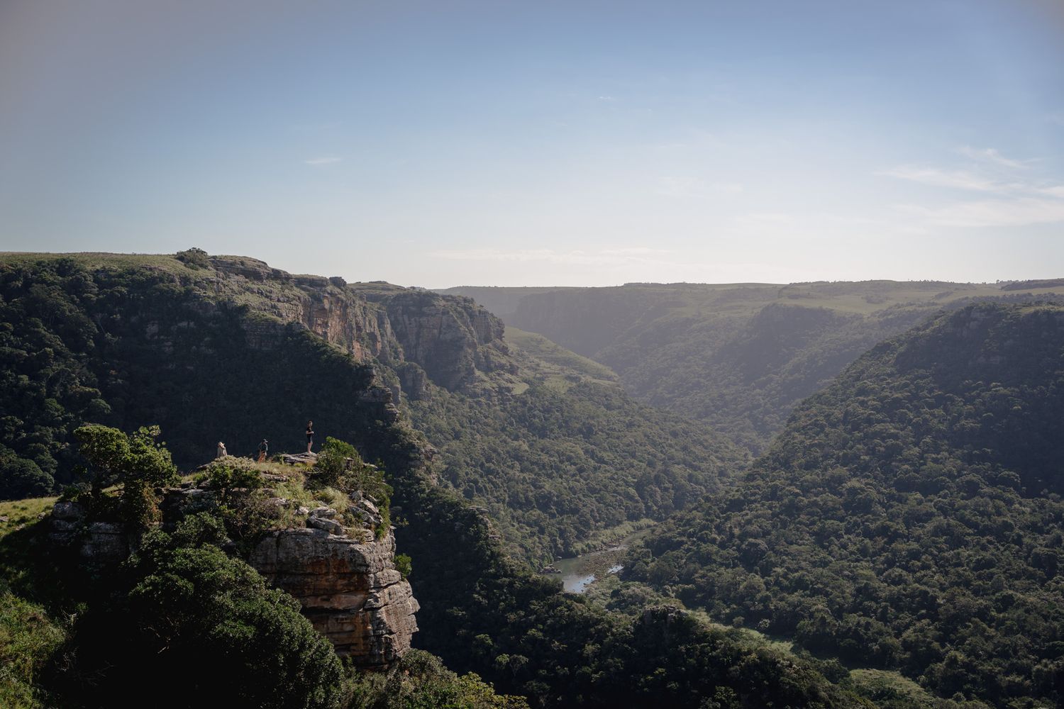 Deep valley surrounded by dramatic cliffs and dense vegetation under blue skies.