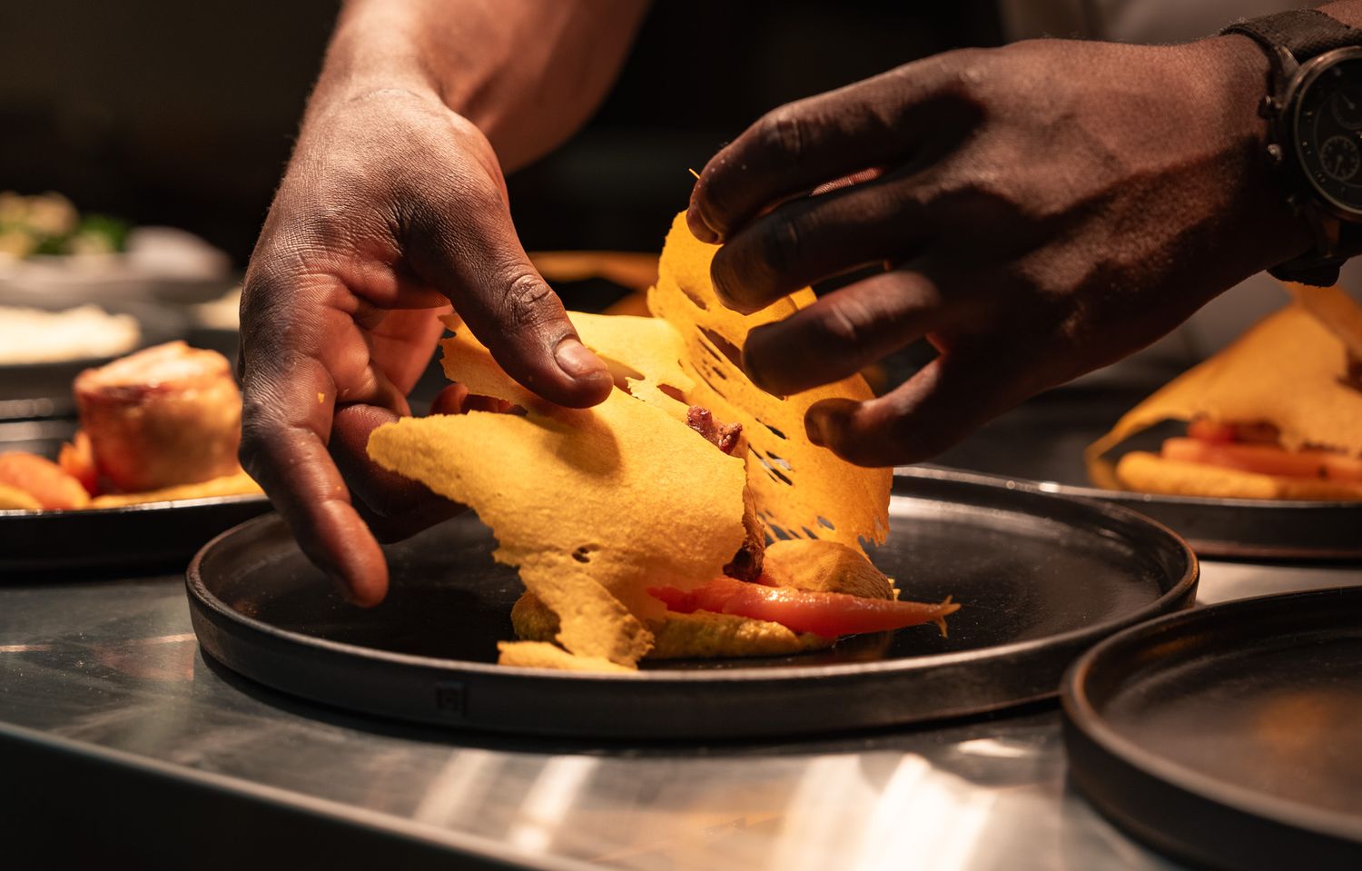 Chef plating sliced orange sweet potatoes on dark plates in a professional kitchen setting.