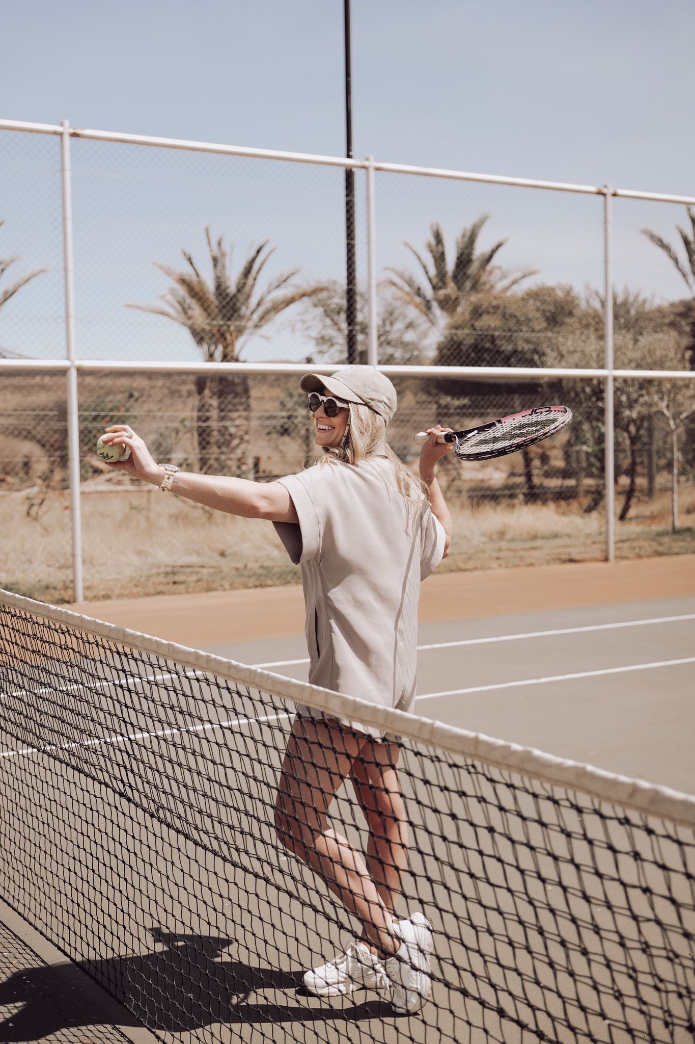 Tennis player on court with palm trees in background during sunny day.
