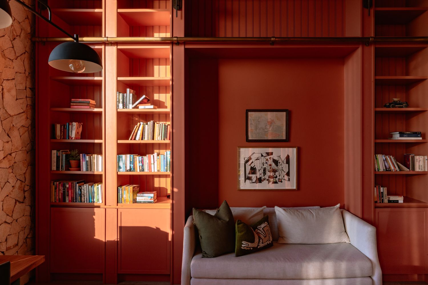 Modern library interior with red walls and built-in wooden shelving displaying books.