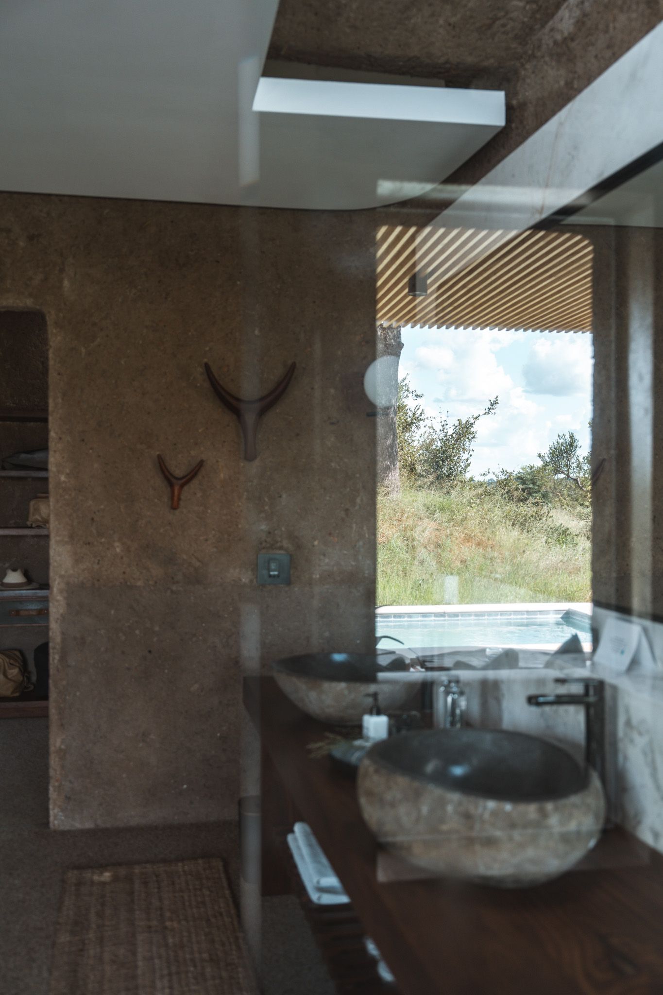 Modern bathroom interior with stone sink and natural textures features scenic window view of grassland.