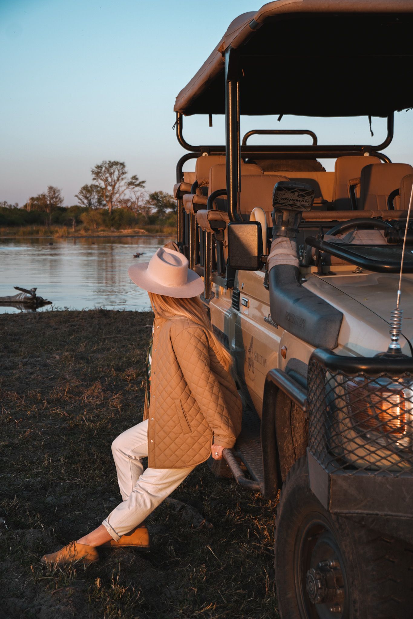 Safari vehicle parked along riverside during golden hour.