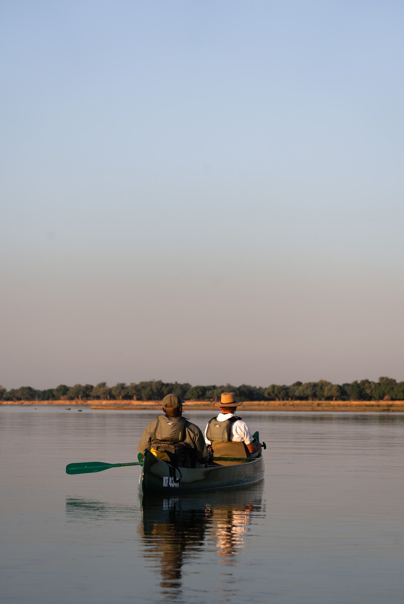 Two people canoeing on calm waters at dusk with reflection on the surface.