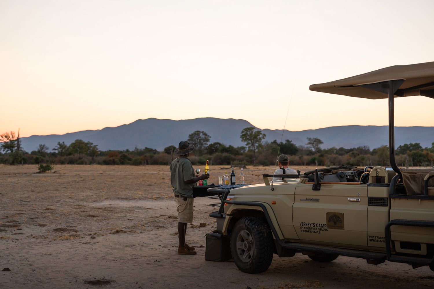 Safari vehicle parked in African wilderness with mountains in background at sunset.