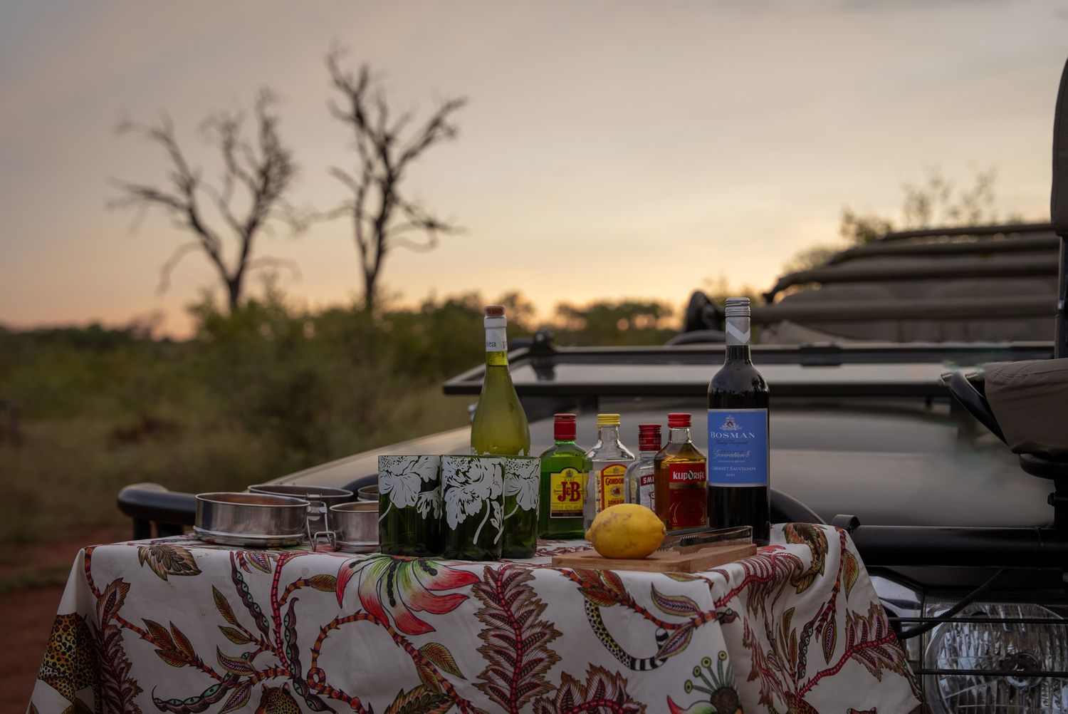 Rustic outdoor table setting with drinks and snacks at sunset.