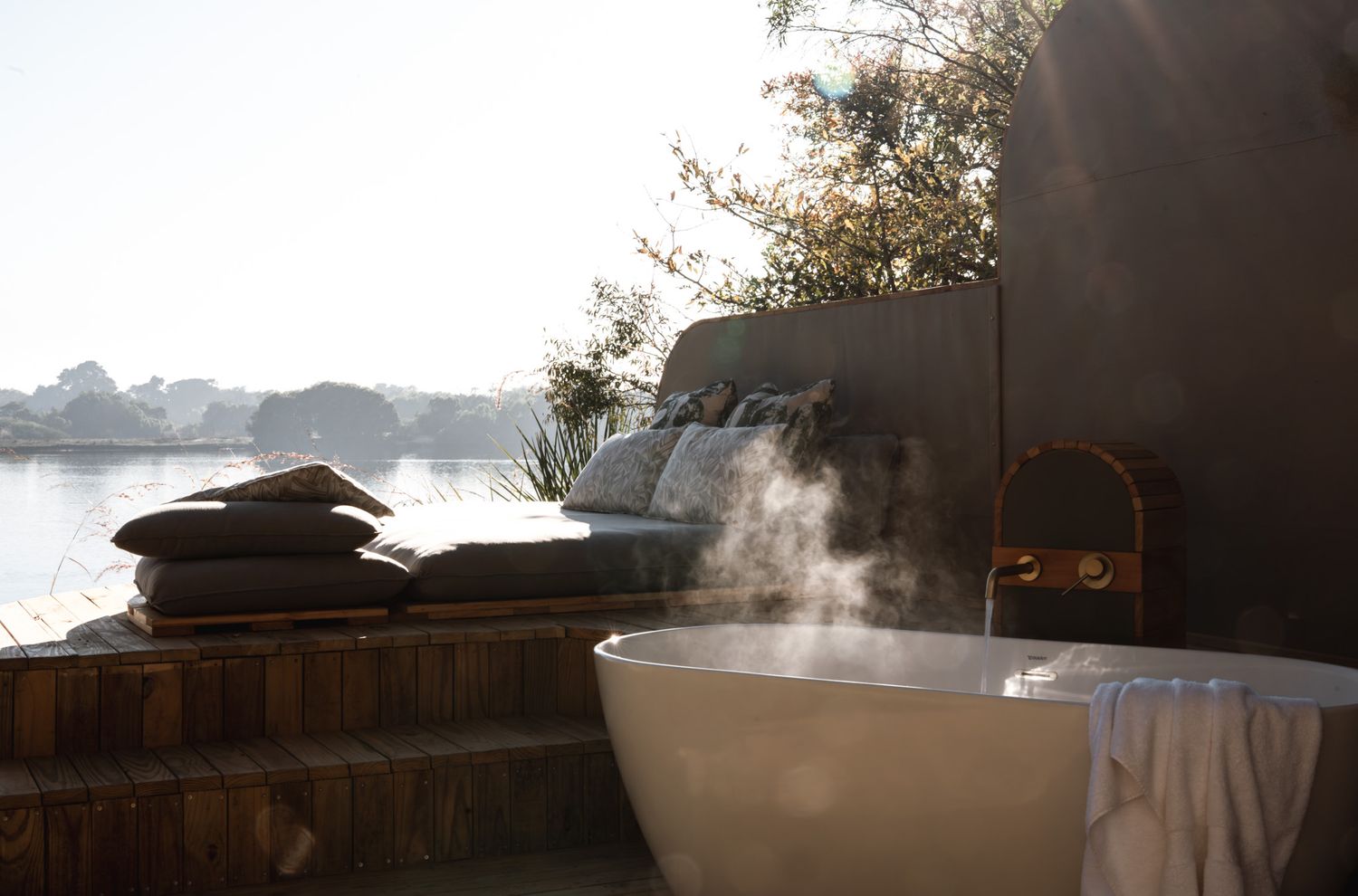 Steaming outdoor bathtub at dusk overlooking a serene waterfront.