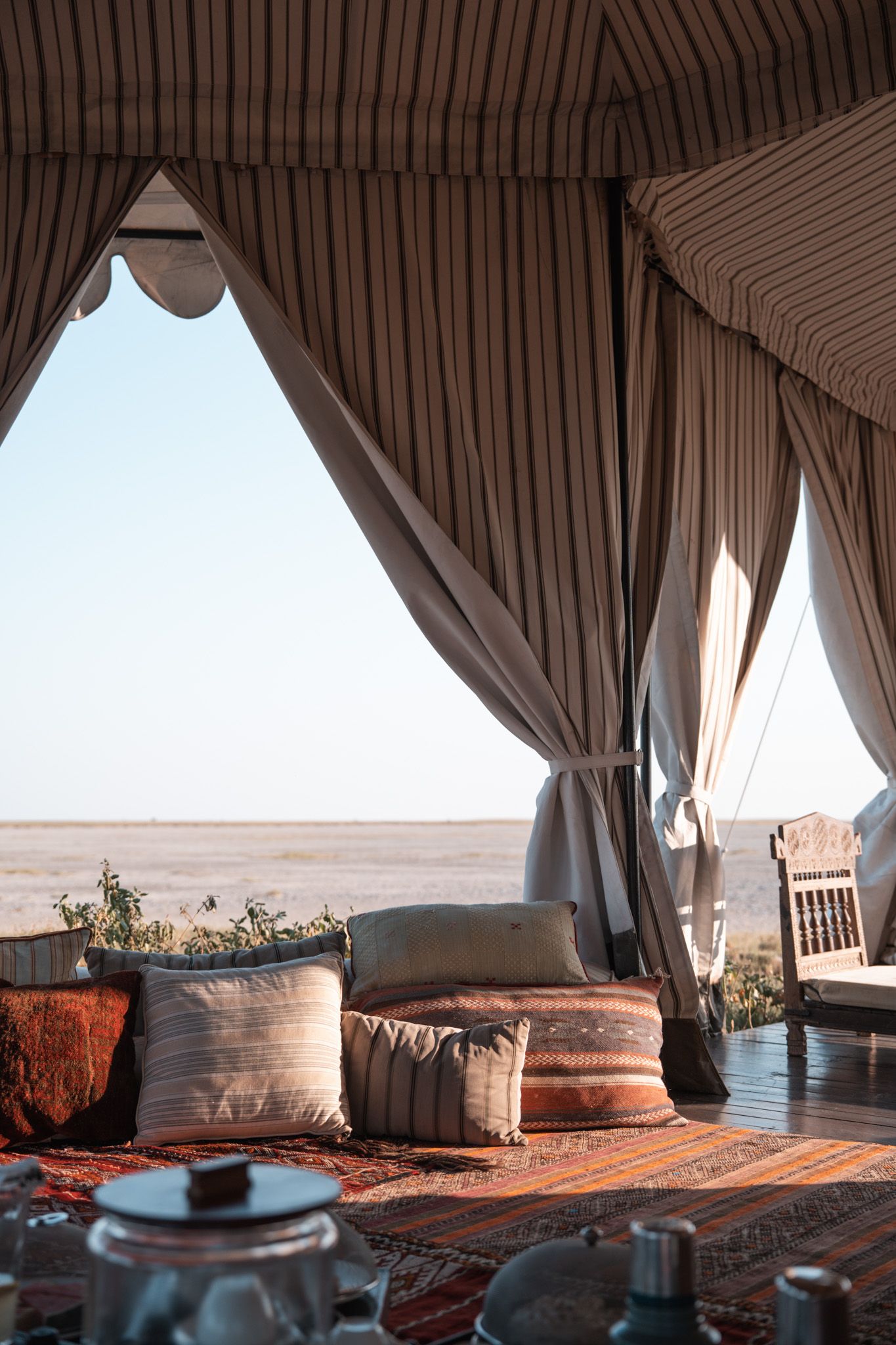 Luxury desert tent interior with draped curtains and cushions overlooking a sandy landscape.