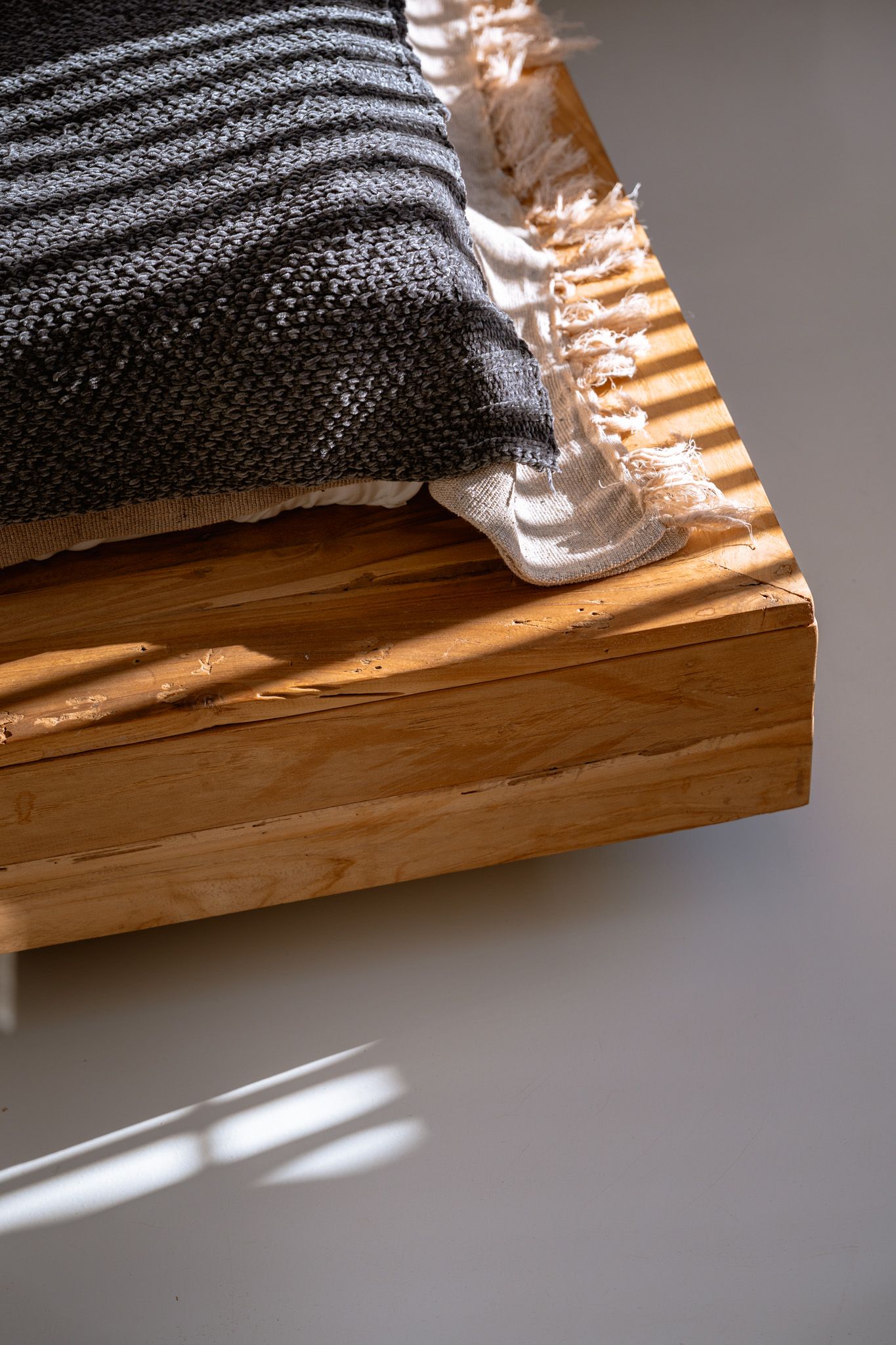 Striped gray blanket with sunlight patterns resting on wooden surface in natural lighting.