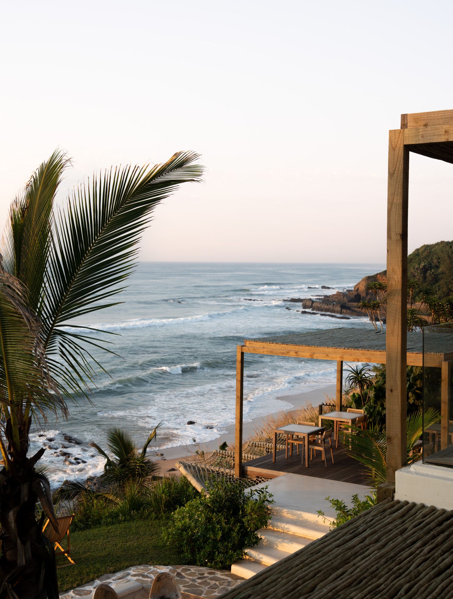 Oceanfront terrace with wooden pergola framing a dramatic coastal view and palm trees.