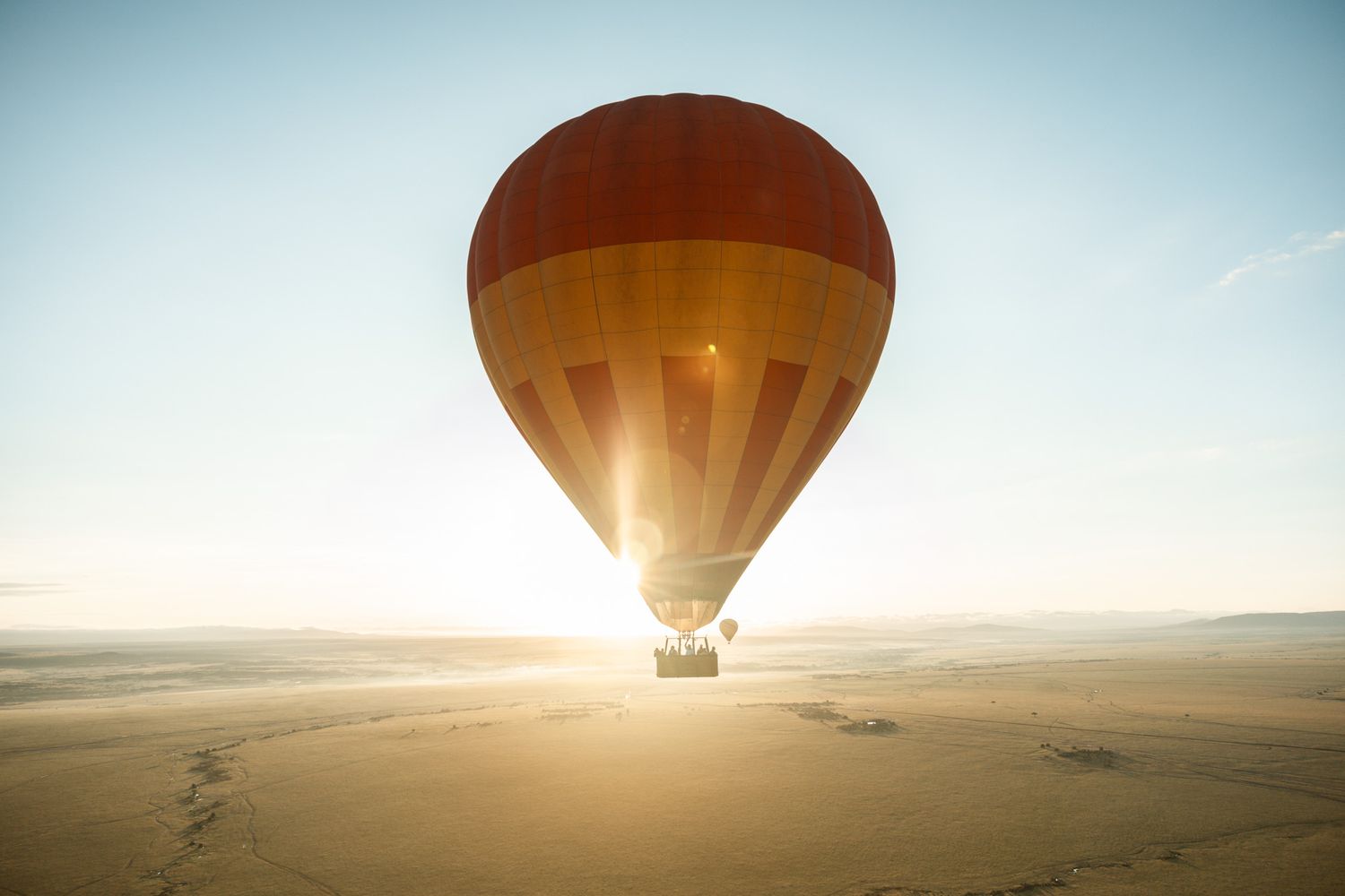 Hot air balloons silhouetted against a bright desert sunrise sky.